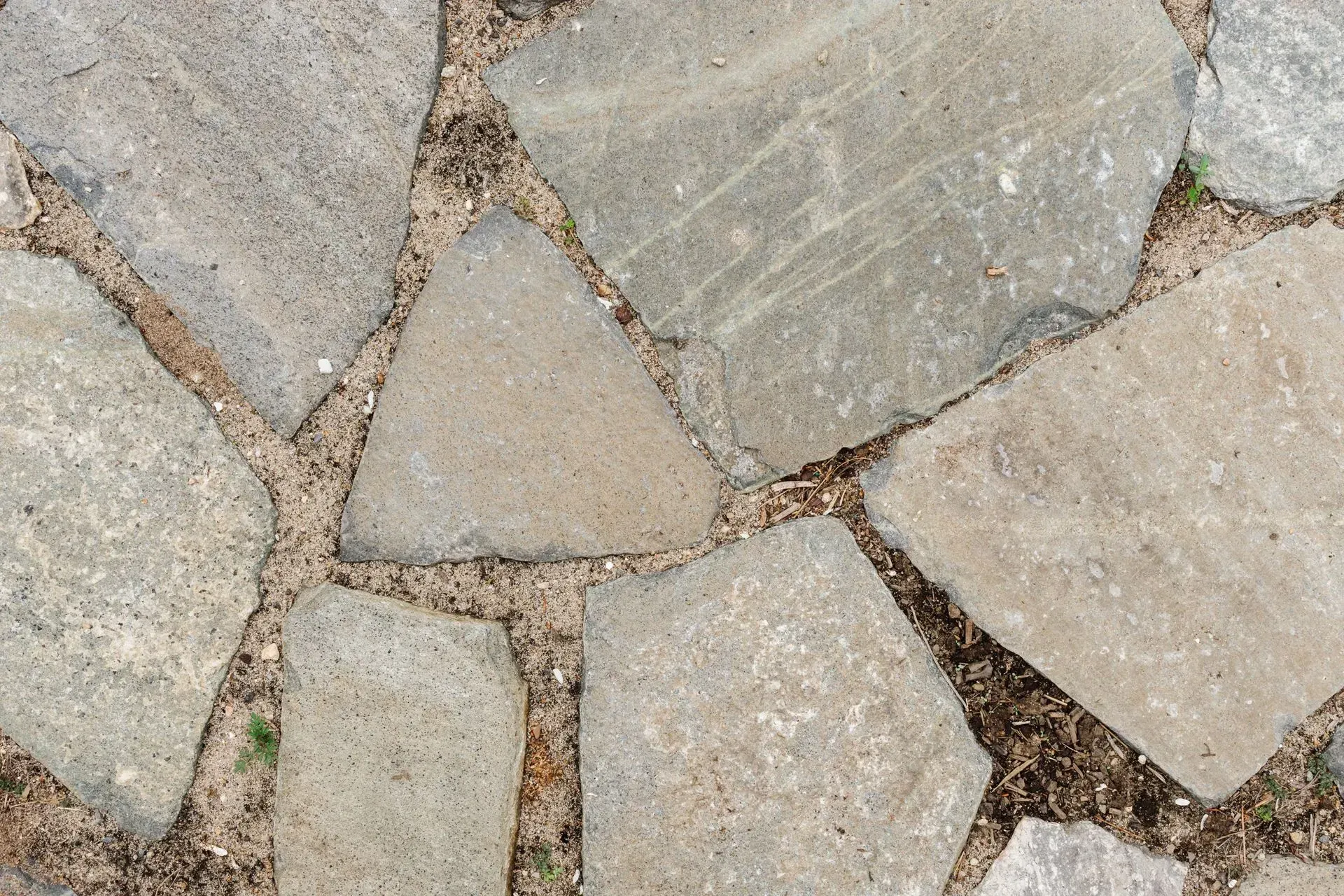 Close-up of light gray stone paving with irregular slabs and brown mortar lines