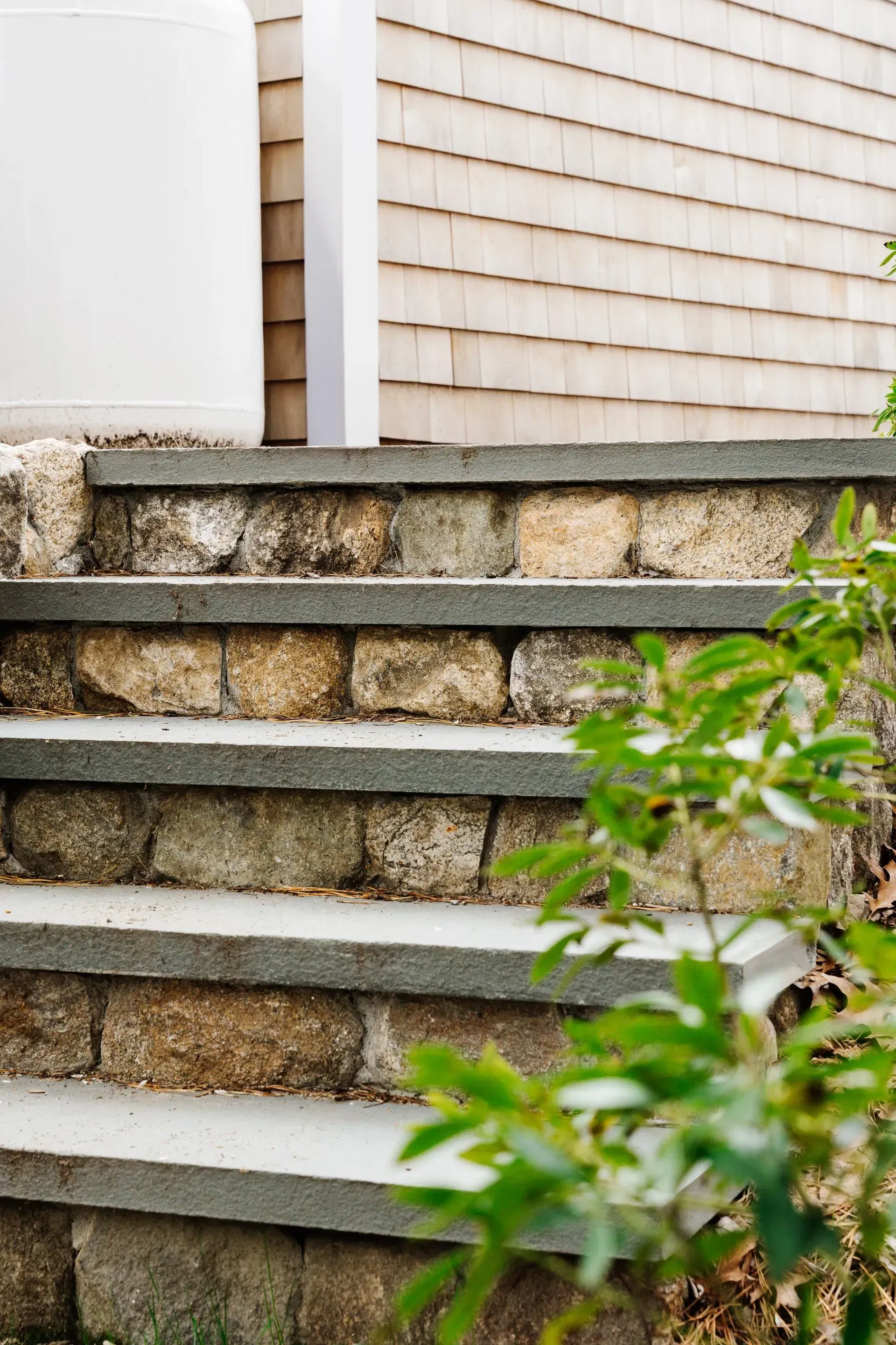 Stone front steps beside a house with beige siding and green shrubs in the foreground