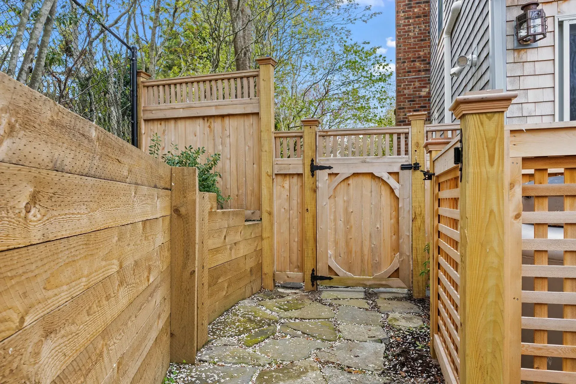 Narrow stone path between wooden fences leading to a small round-topped gate in a backyard.
