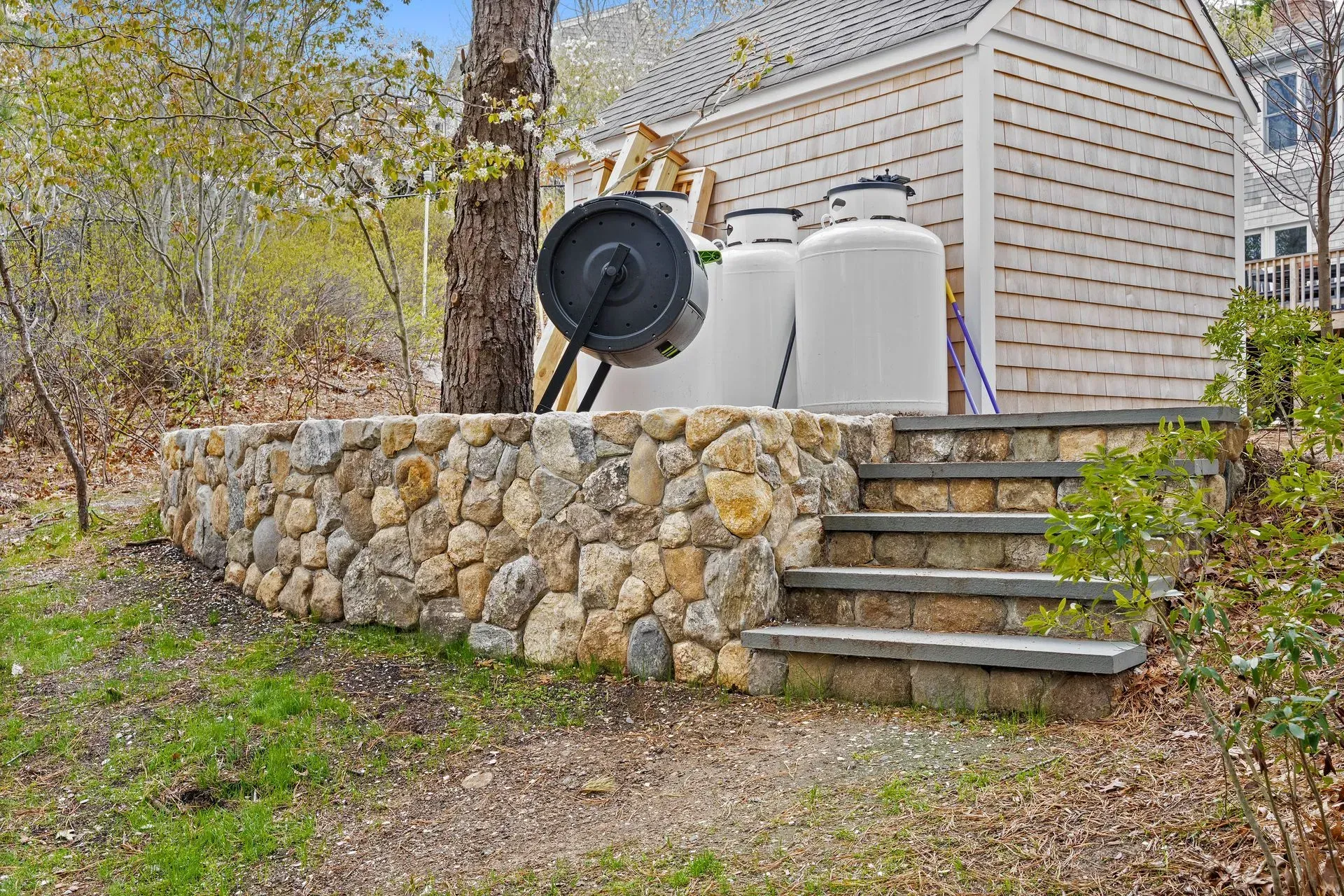 Stone steps beside a stone retaining wall leading to a house with a grill and storage tanks outdoors