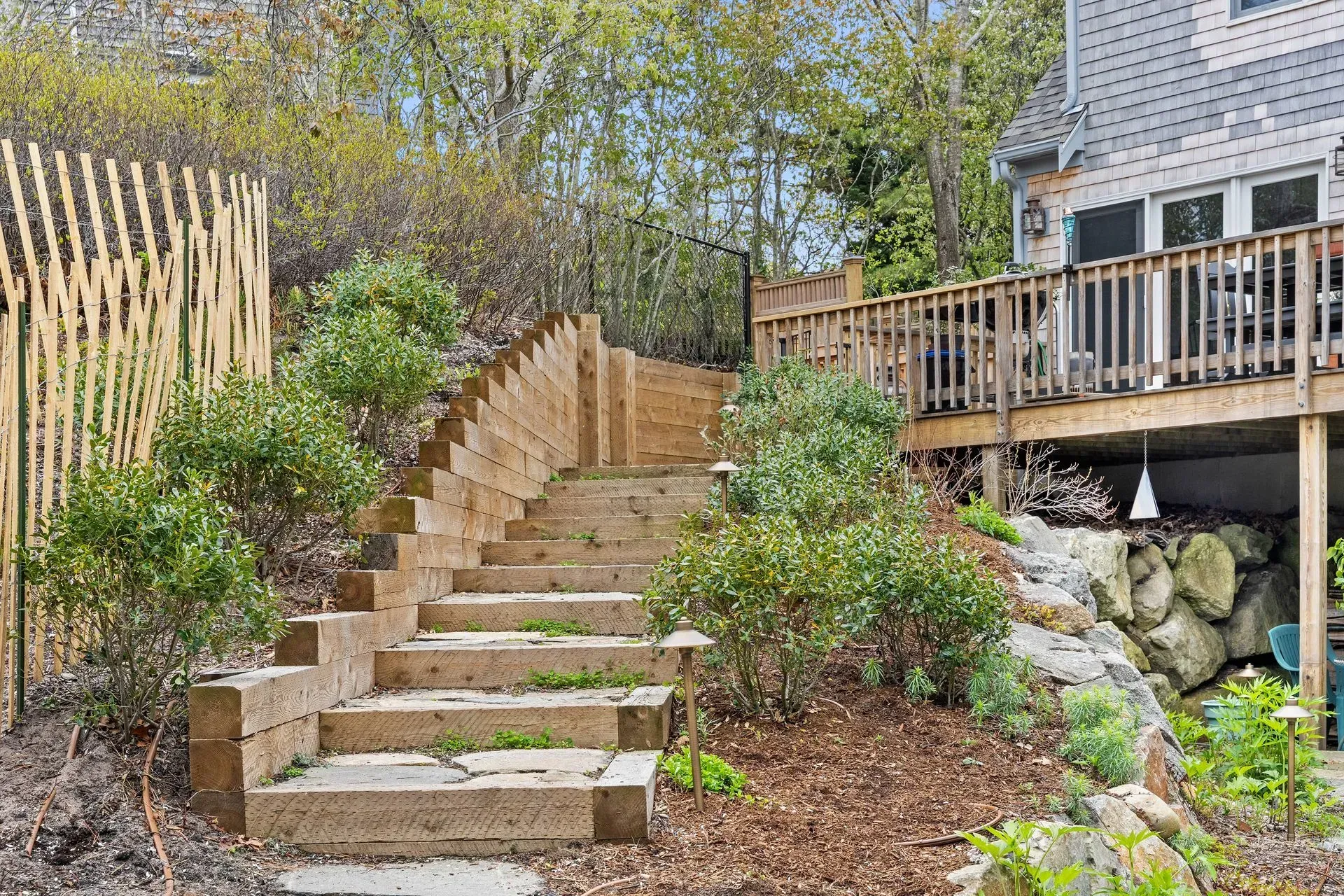 Stone steps through a landscaped garden beside a wooden deck and house.
