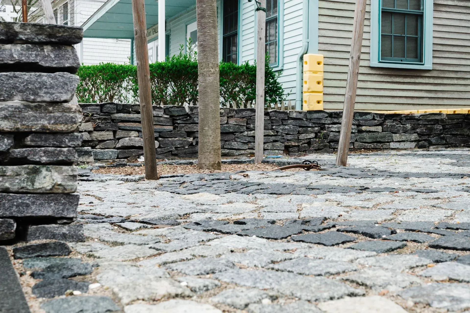 Stone-paved courtyard with trees, stone wall, and a house in the background