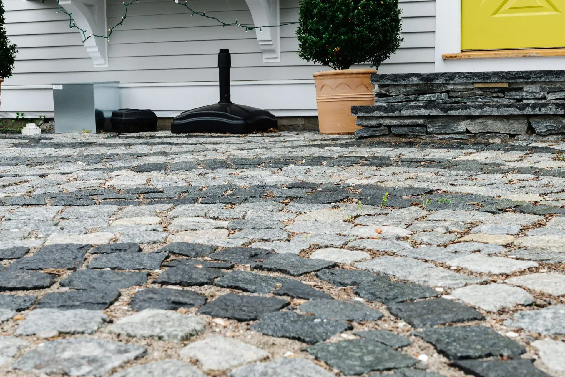 Cobblestone patio in front of a white house with stone steps, potted plant, and broom handle near the wall
