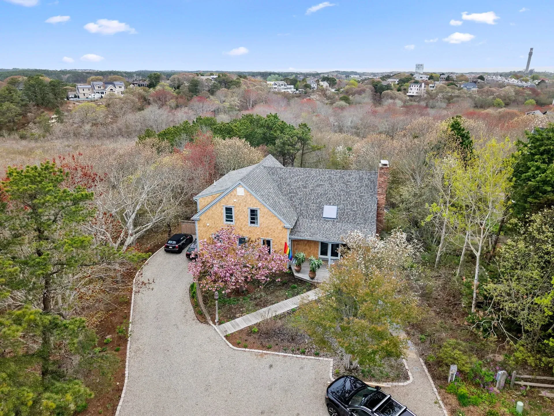Aerial view of a stone house with a curved driveway and spring trees in bloom under a blue sky