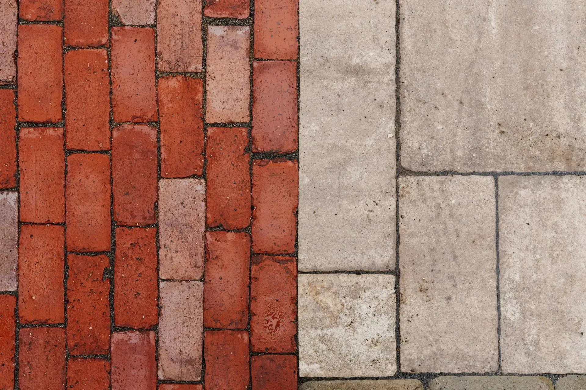 Red brick pavers beside light gray stone paving in a close-up ground pattern.