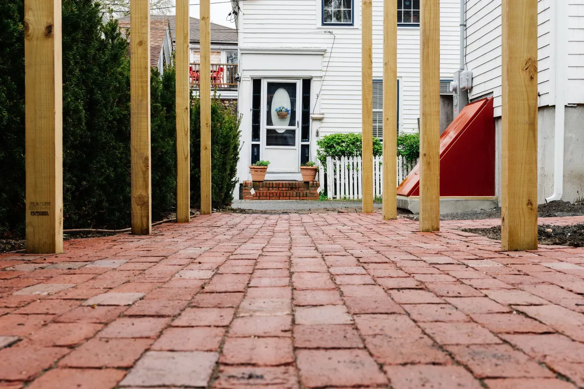 Brick walkway leading to a white house doorway, lined with wooden posts and a red bench