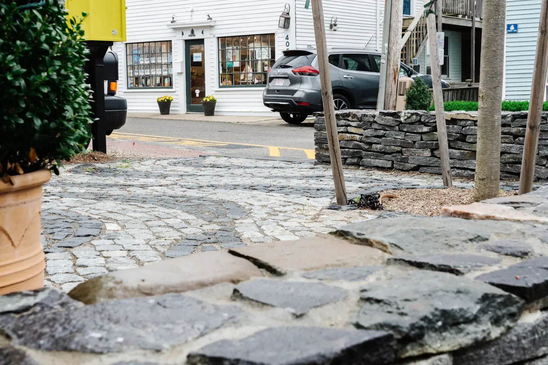 Stone path leading to a street with parked cars and a white building behind a low stone wall.