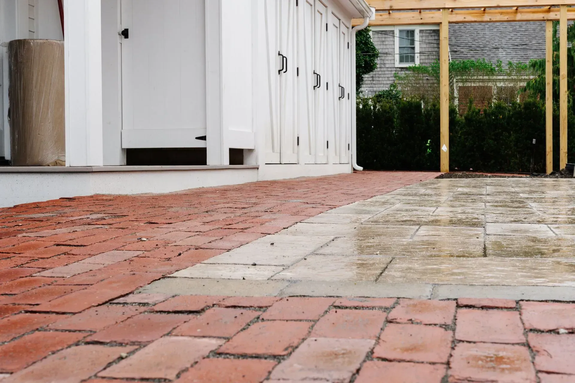 Brick path beside white outdoor cabinets and a wet patio with wooden fence in the background