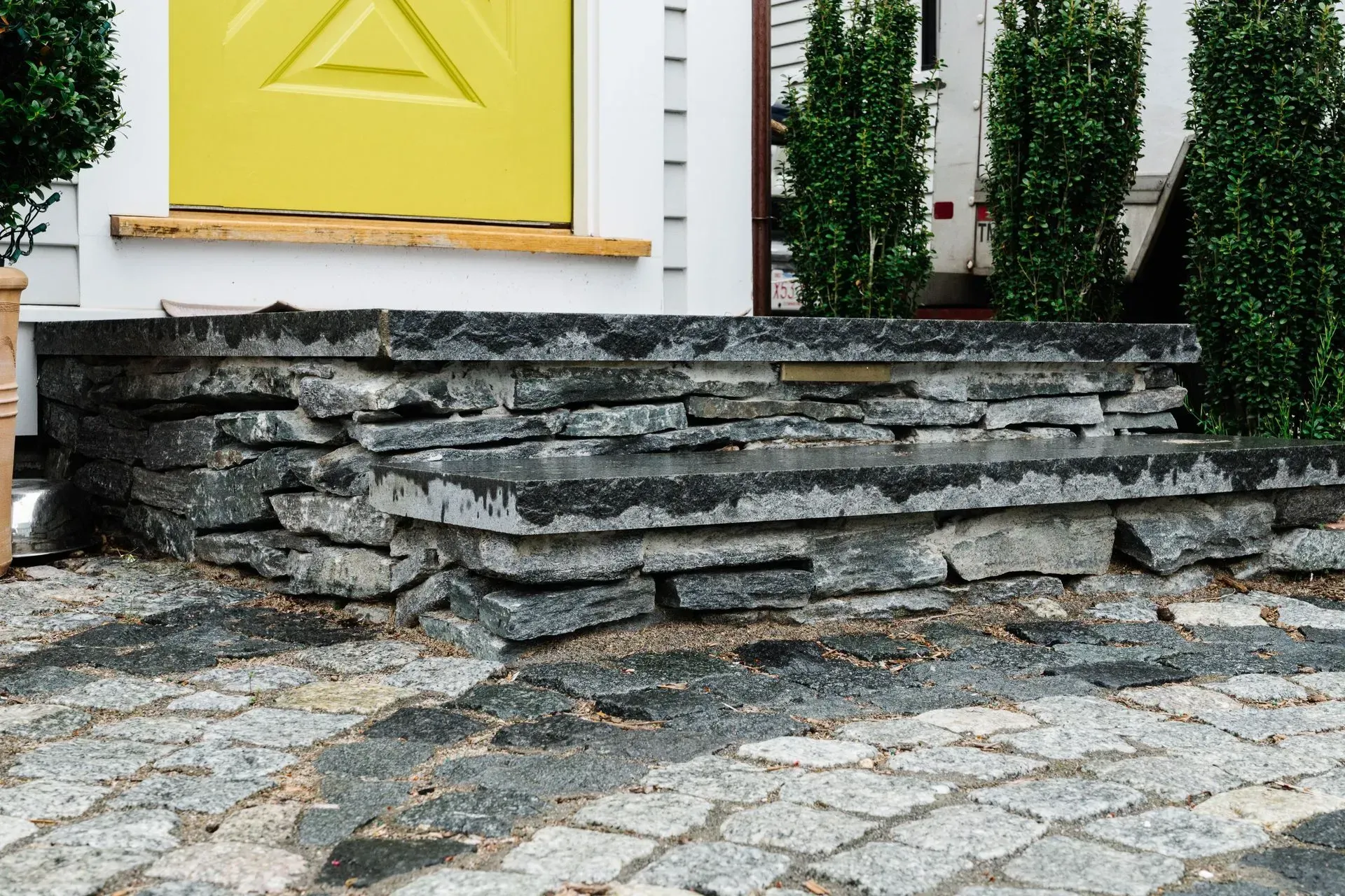 Stone steps leading to a yellow front door with cobblestone path in front