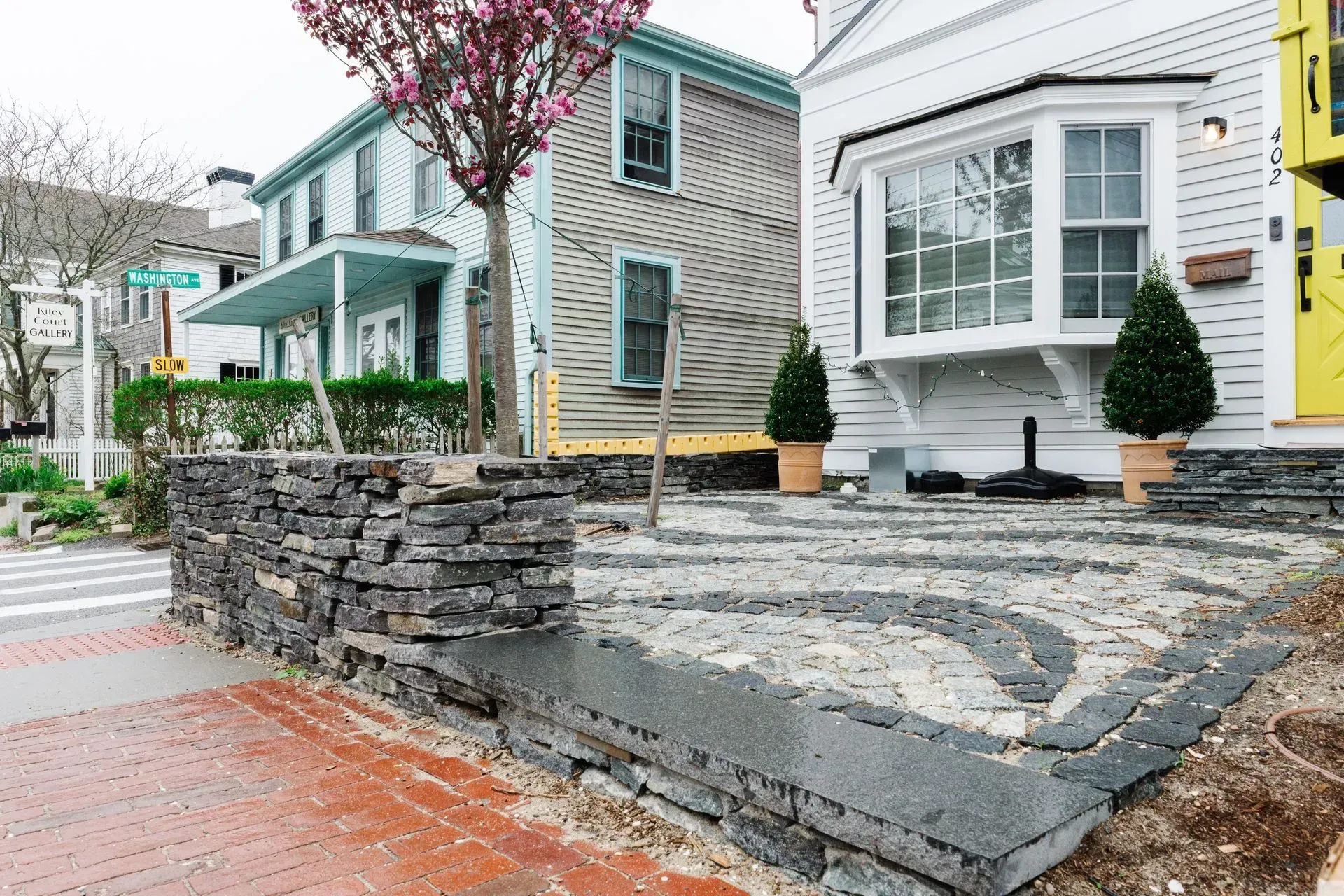 Residential houses with stone retaining wall, paved sidewalk, and pink flowering tree in front yard