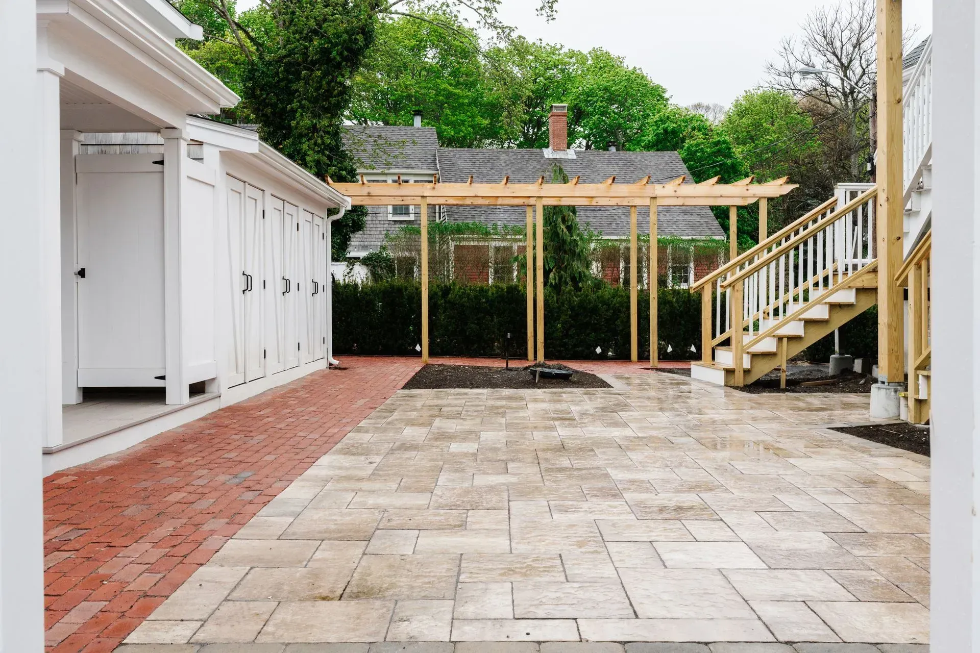 Backyard patio with paver stones, pergola, and wooden stairs beside a house