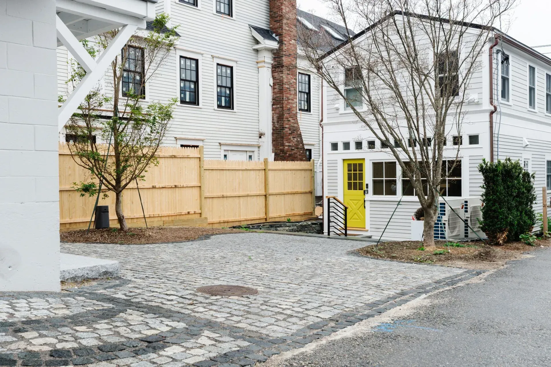White houses with a yellow door beside a cobblestone driveway and bare trees
