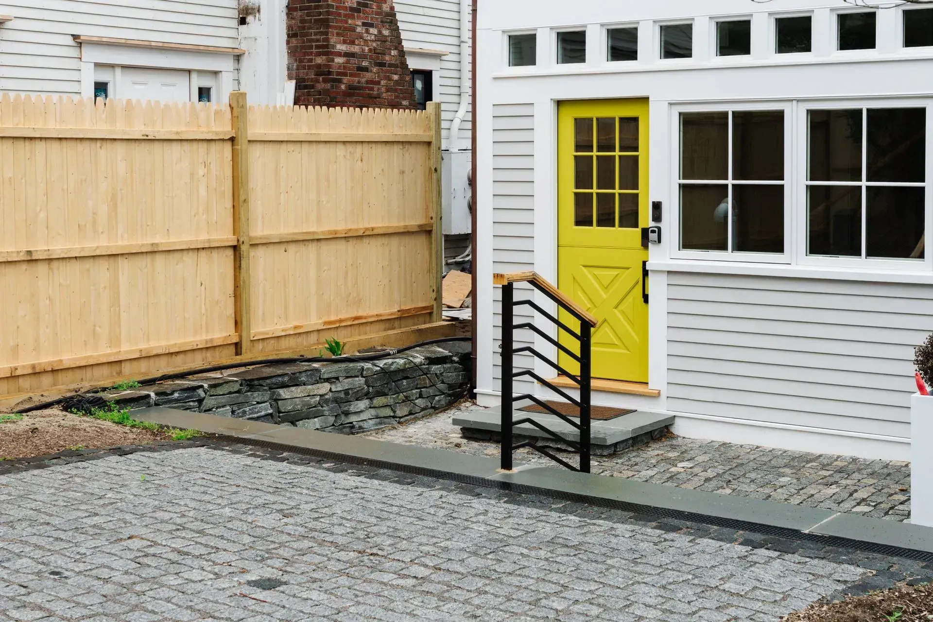 Yellow back door with steps and black railing beside a fenced gravel patio.