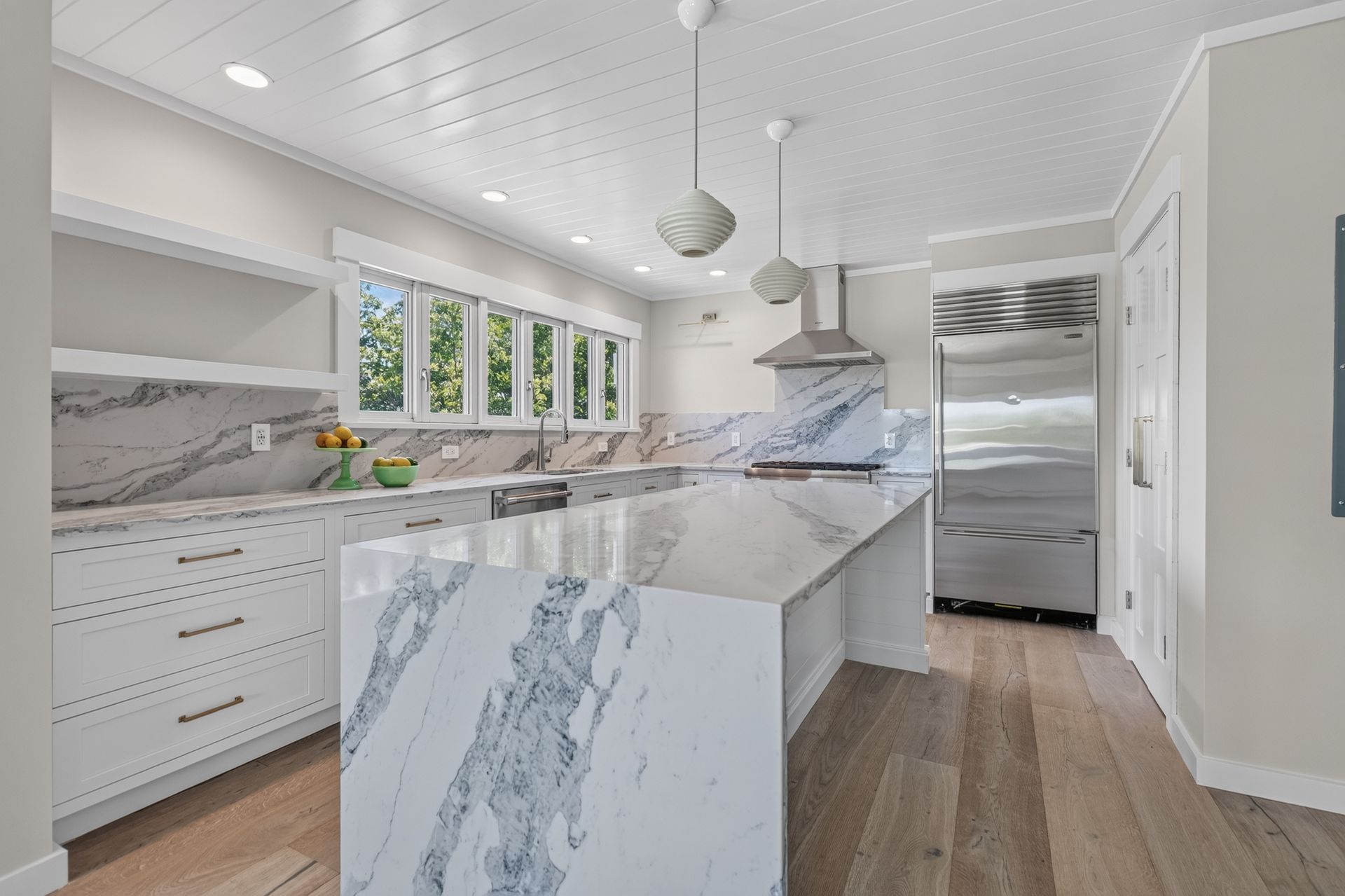 Bright modern kitchen with marble island, white cabinets, pendant lights, and stainless-steel appliances
