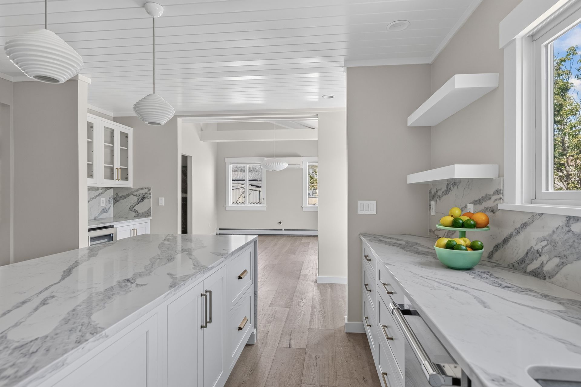 Bright white kitchen with marble countertops, light wood floors, and open shelving