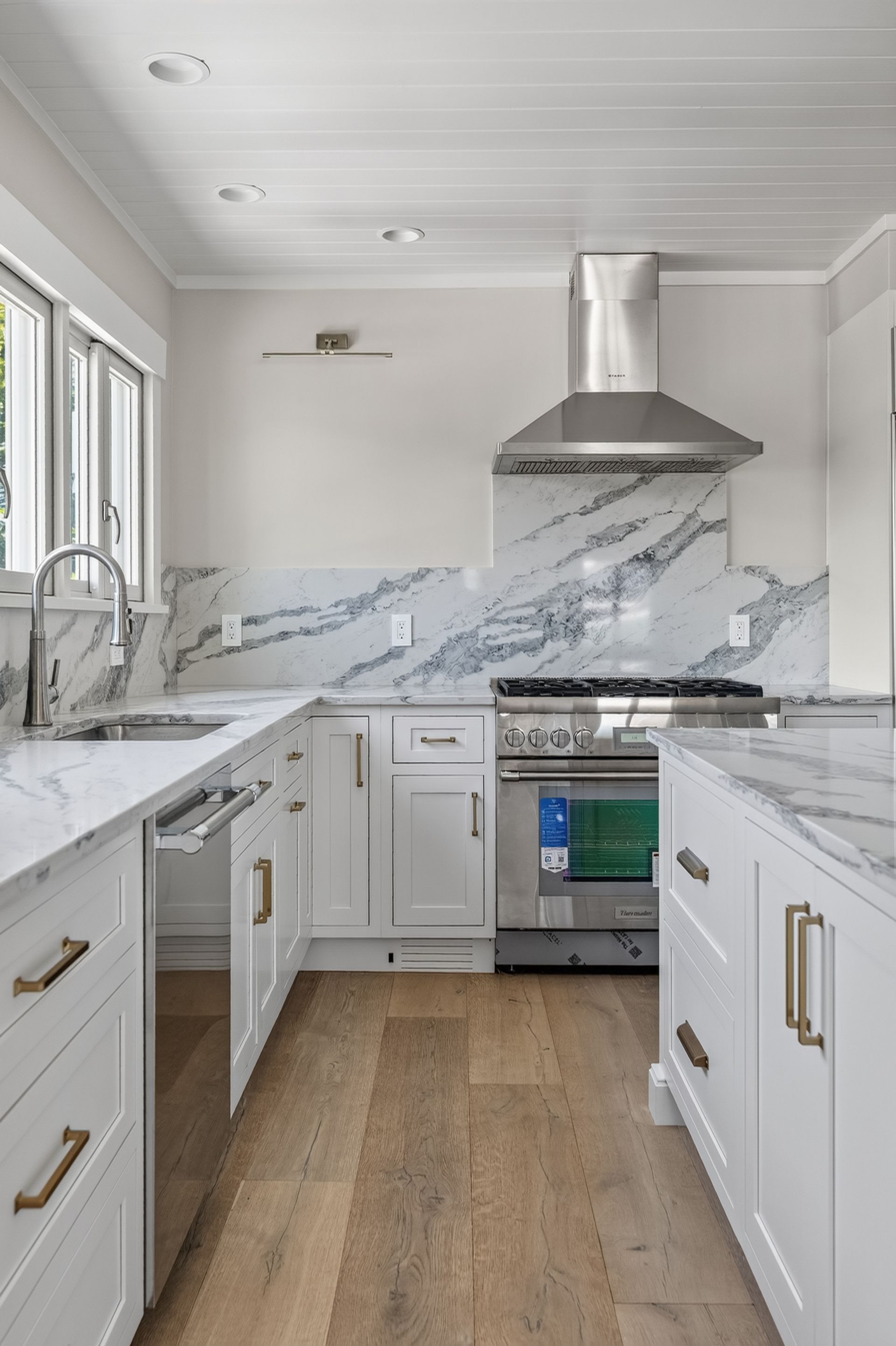 Bright white kitchen with marble countertops, stainless range hood, and wood floor.