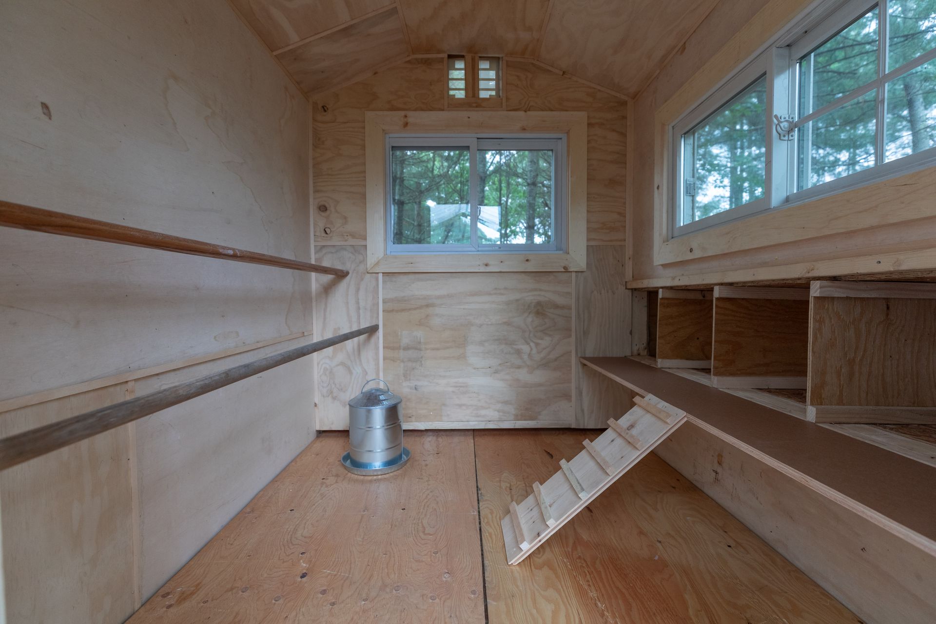 Empty unfinished wooden interior with shelves, windows, and a small ladder on the floor