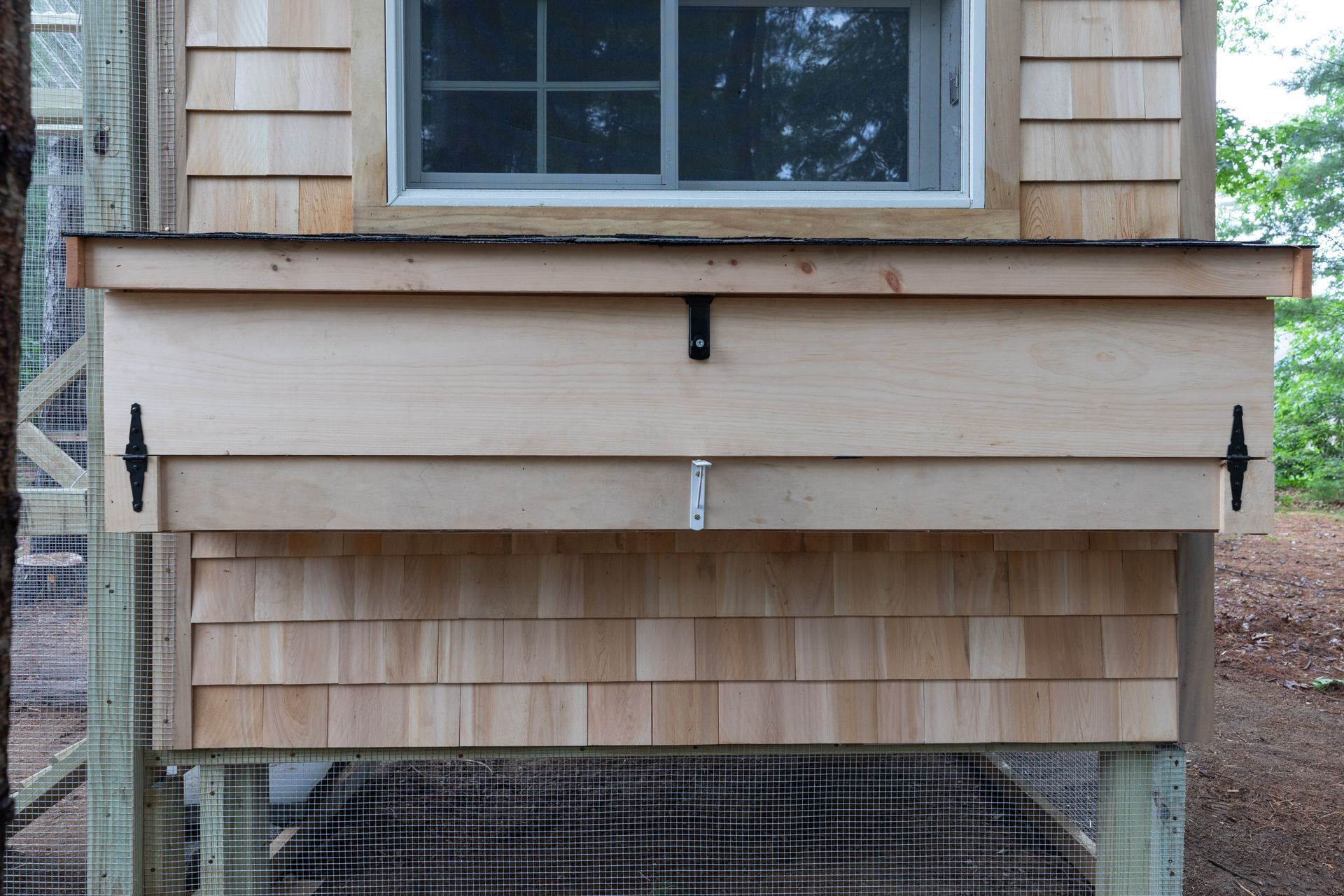 Wooden house exterior with a small front box structure beneath a window and black mesh fabric below