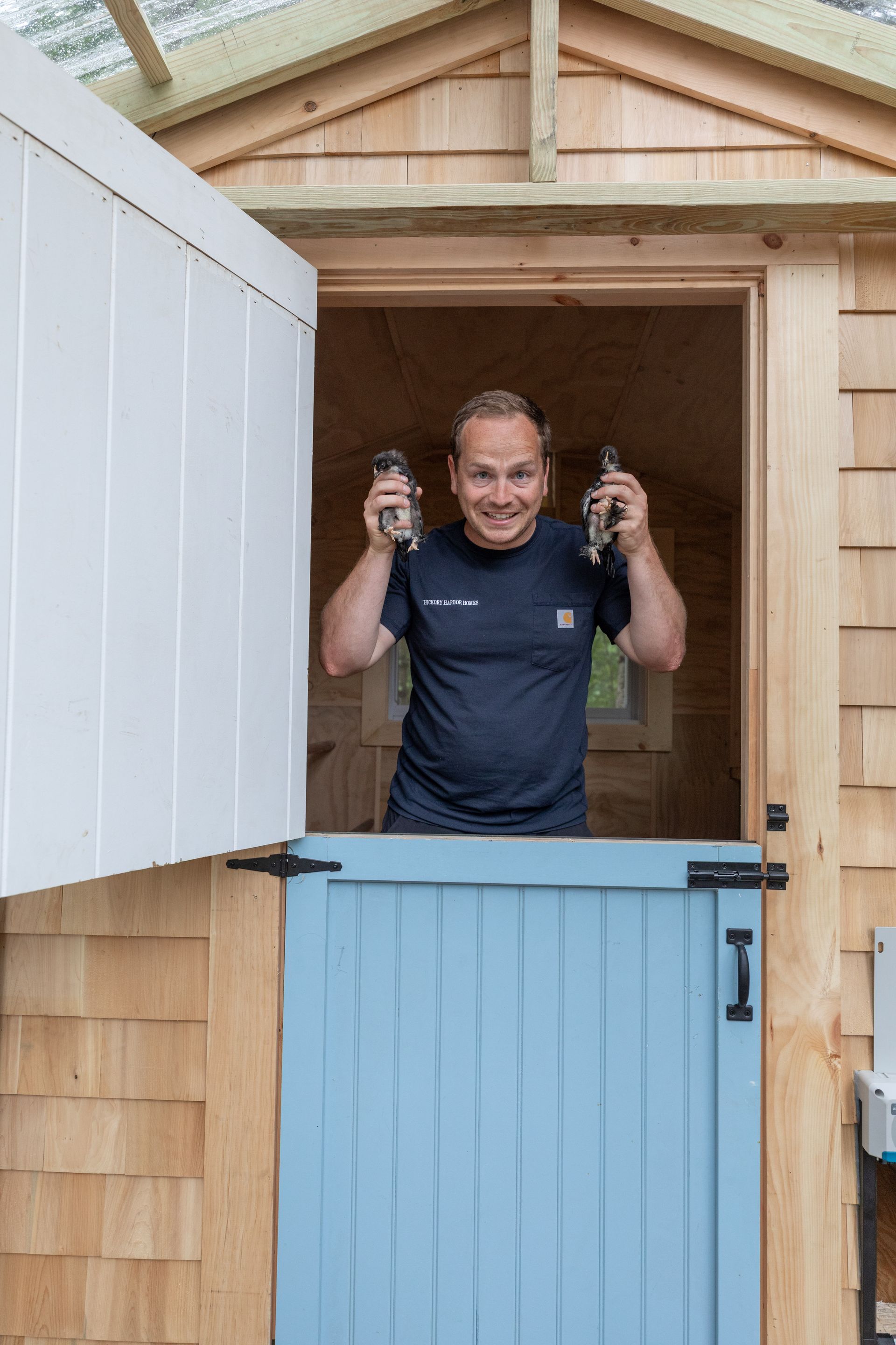 Person in a shed doorway holding up two bottles, behind a blue half-door.