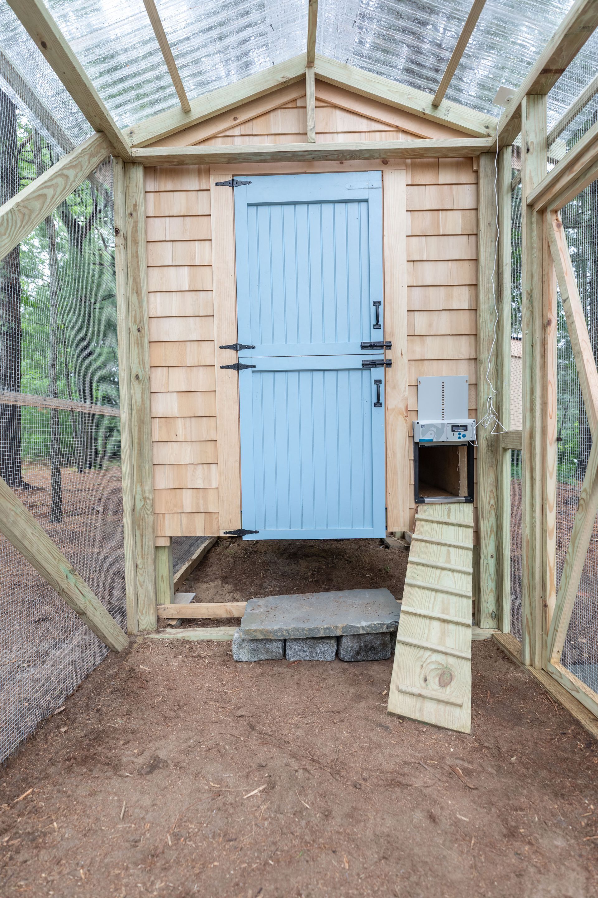 Small greenhouse-like shed with a light blue door, wood framing, and a dirt floor.