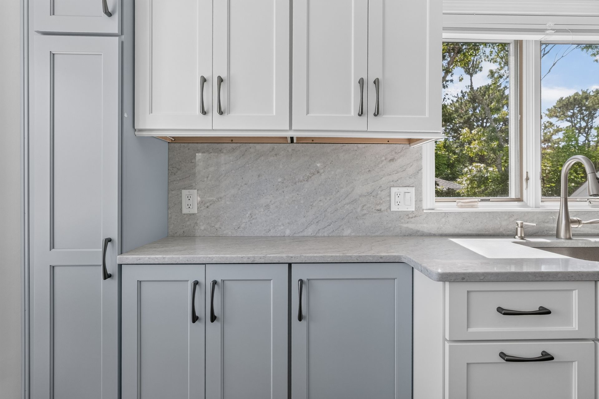 Bright kitchen corner with gray cabinets, white countertops, and a window above the sink