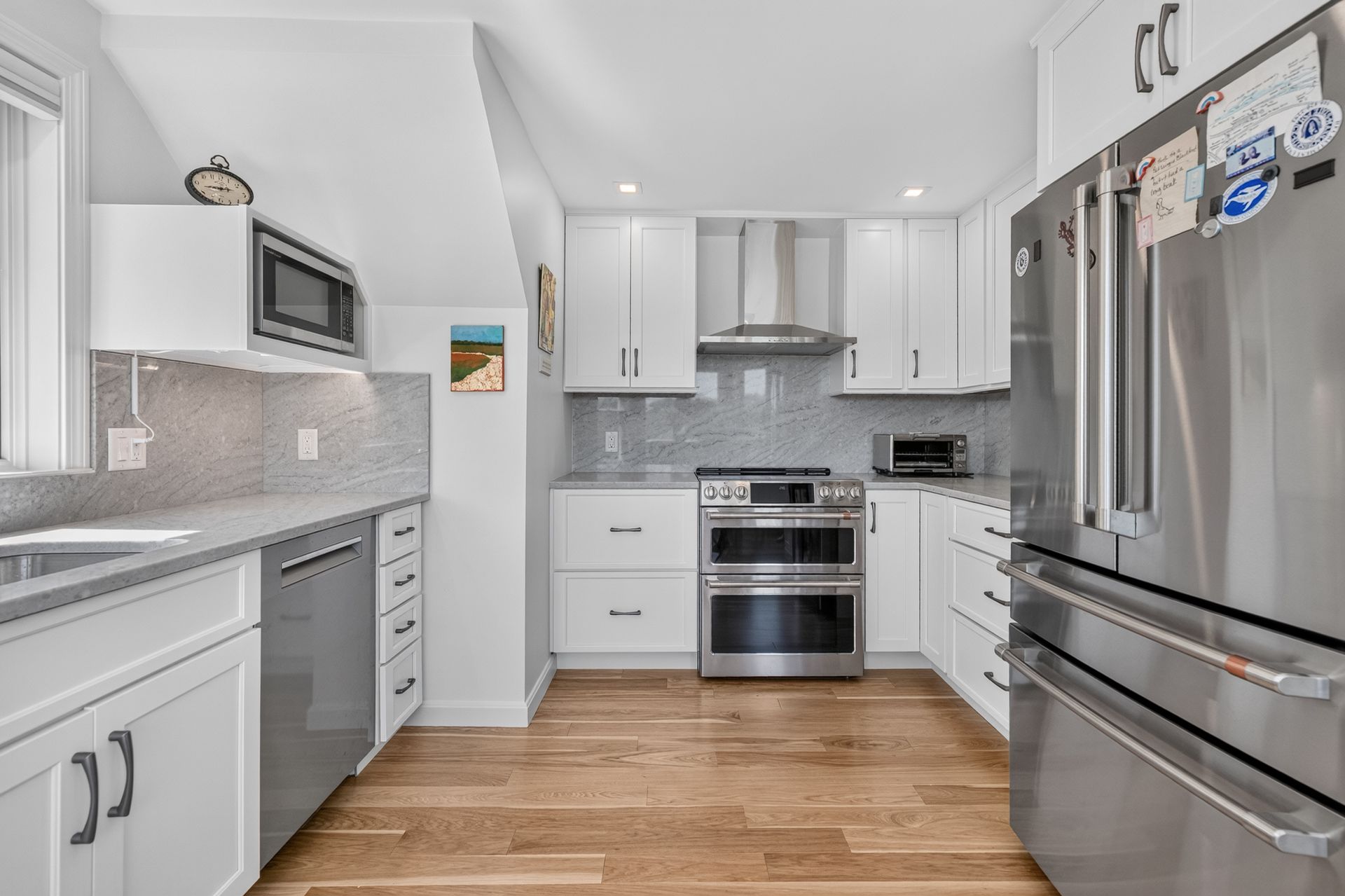 Bright modern kitchen with white cabinets, stainless steel appliances, and hardwood floors