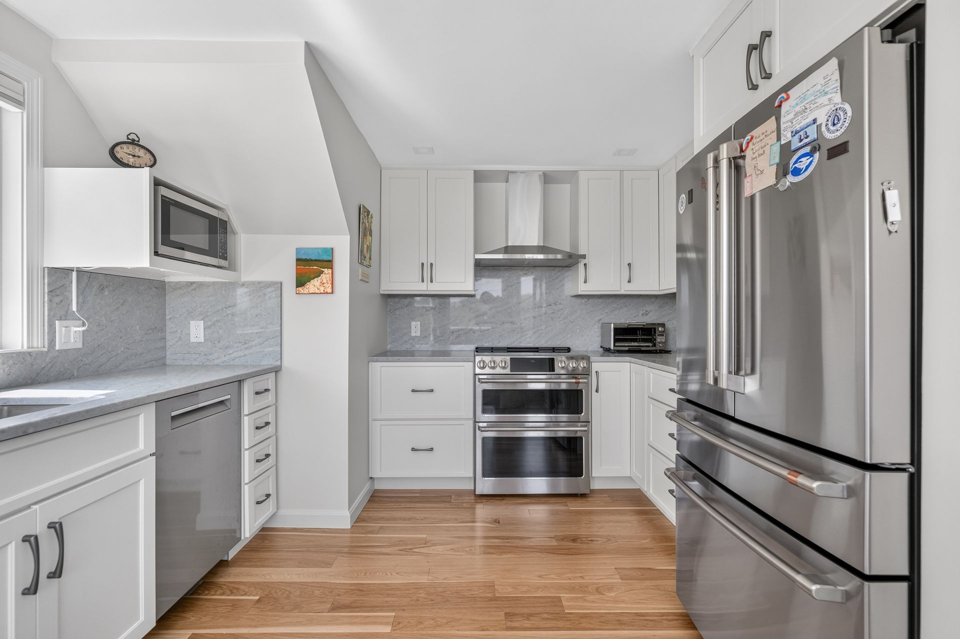 Bright modern kitchen with stainless steel appliances, white cabinets, and wood flooring