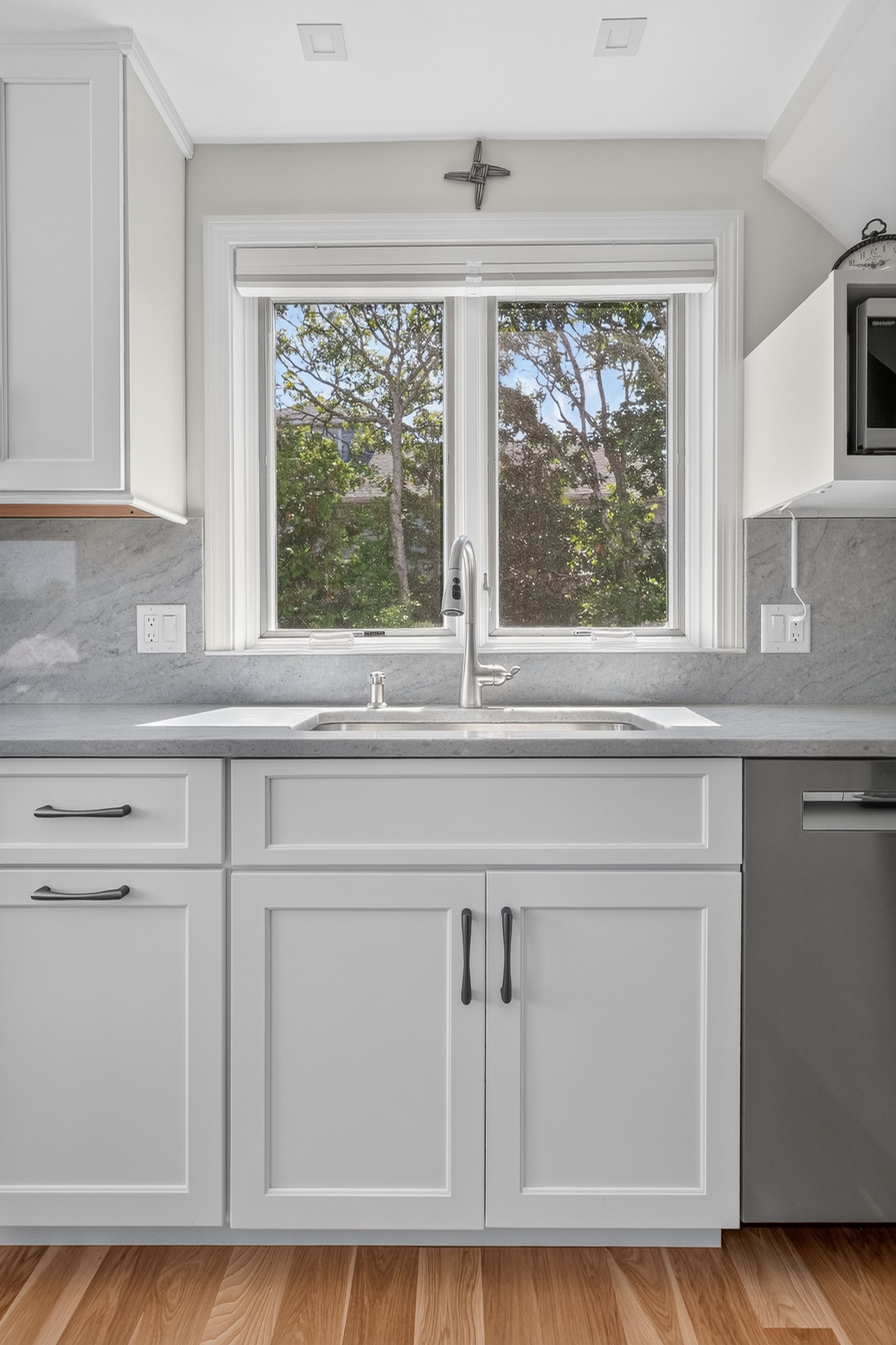 Bright modern kitchen sink with white cabinets and a window overlooking trees
