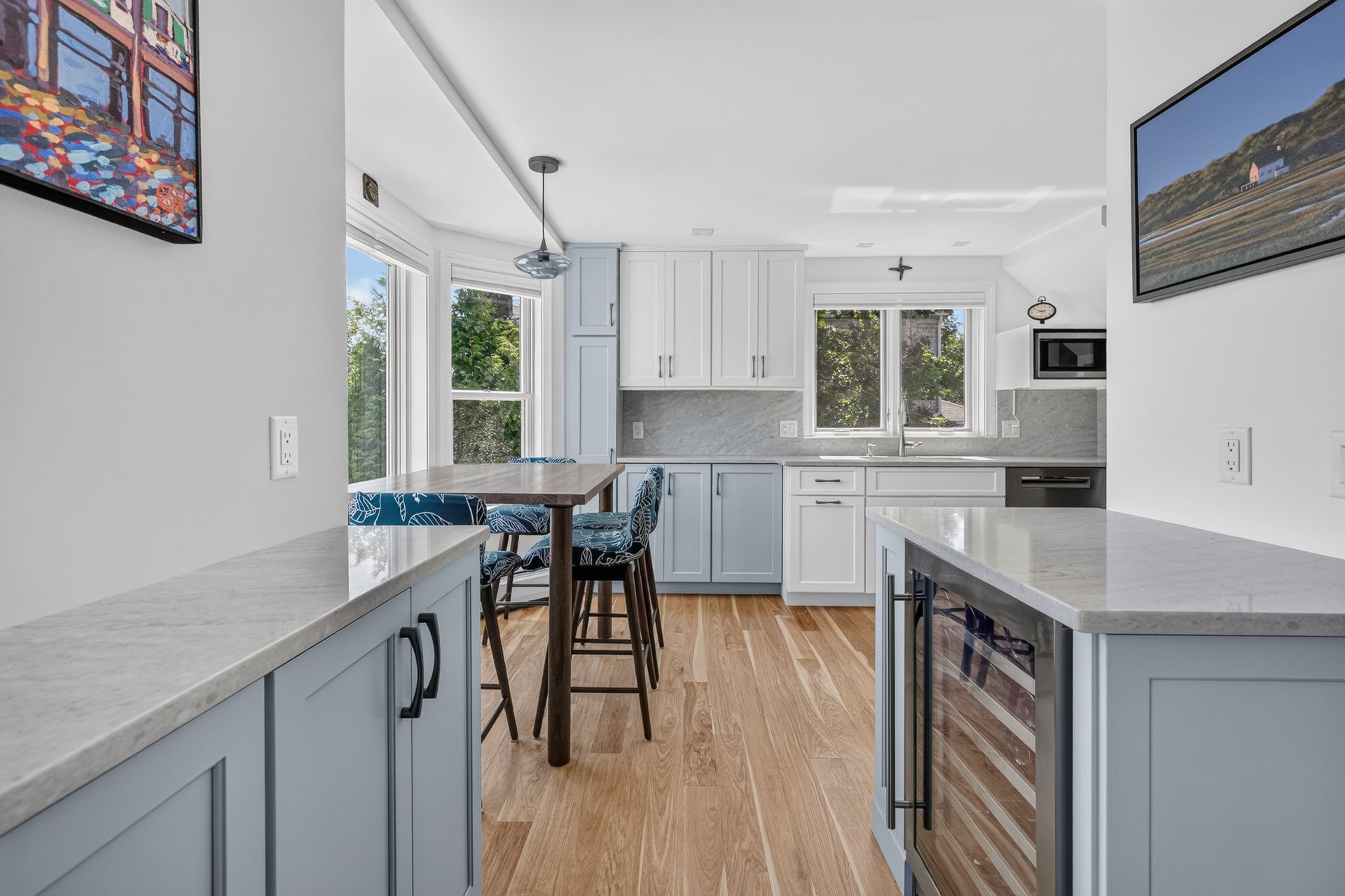 Bright kitchen with blue-gray cabinets, white counters, wood floor, and a small dining table by the window.