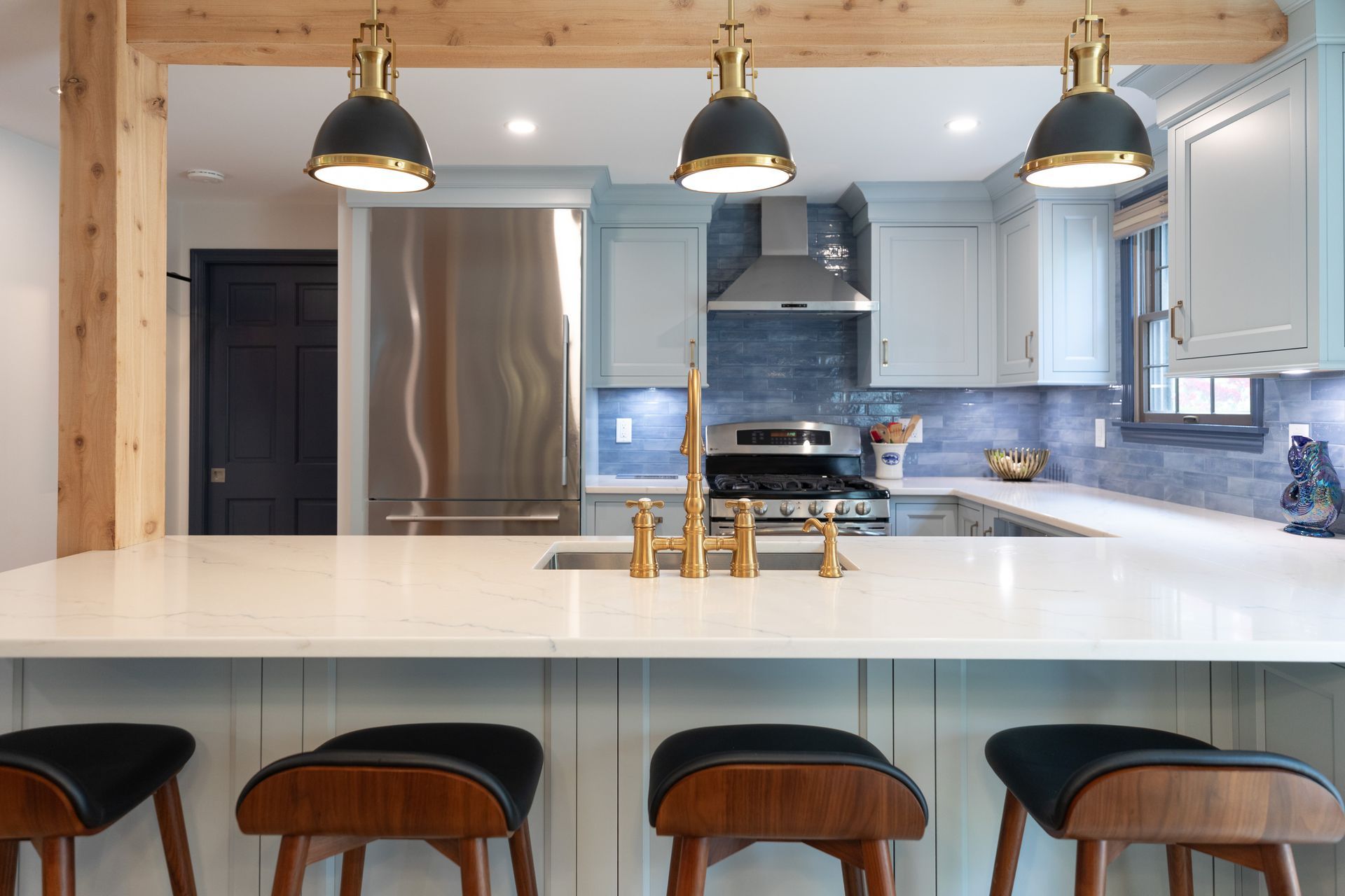 Modern kitchen with island, pendant lights, stainless steel fridge, and black stools in front