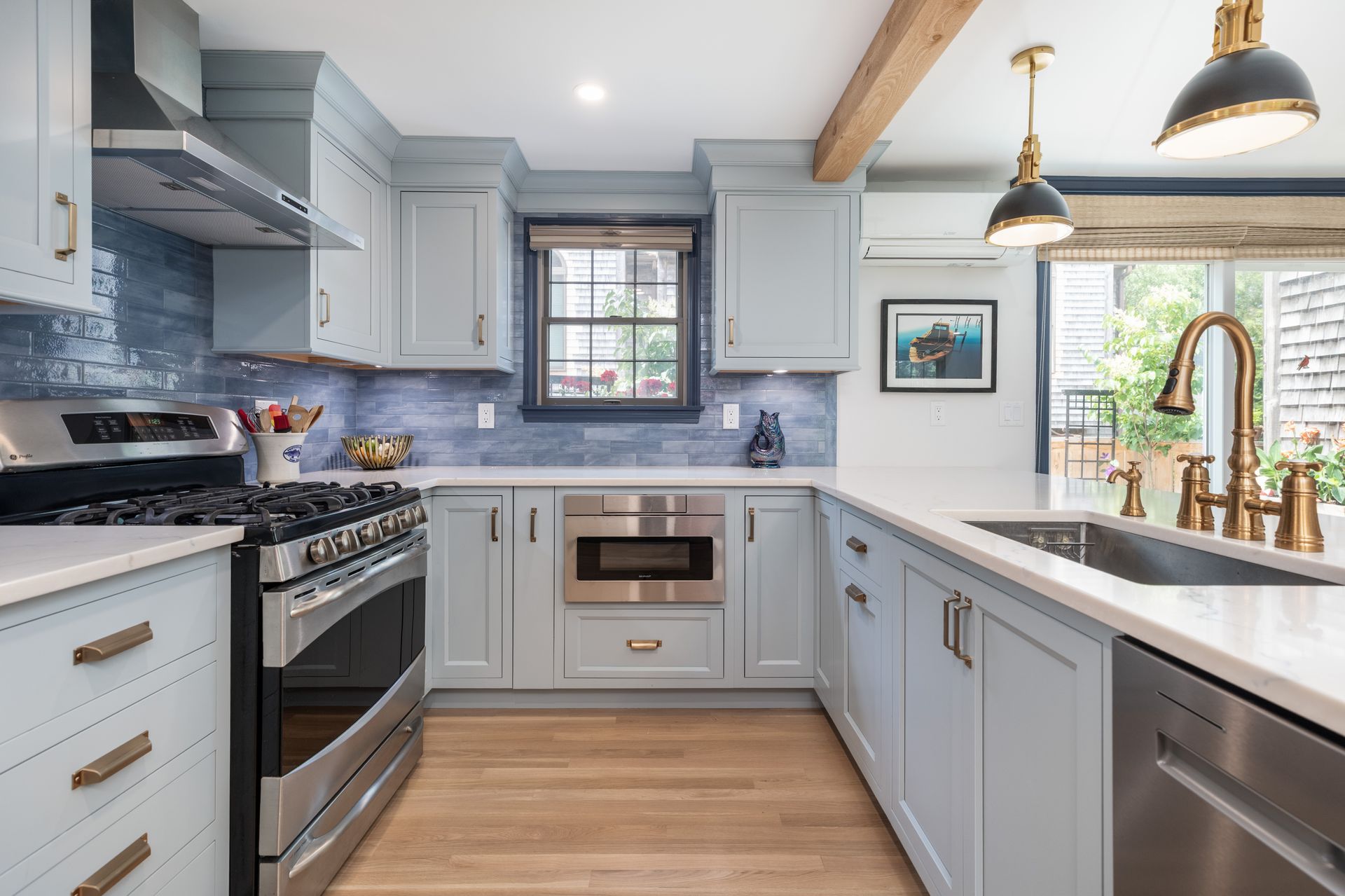 Bright modern kitchen with gray cabinets, stainless steel appliances, wood floor, and pendant lights