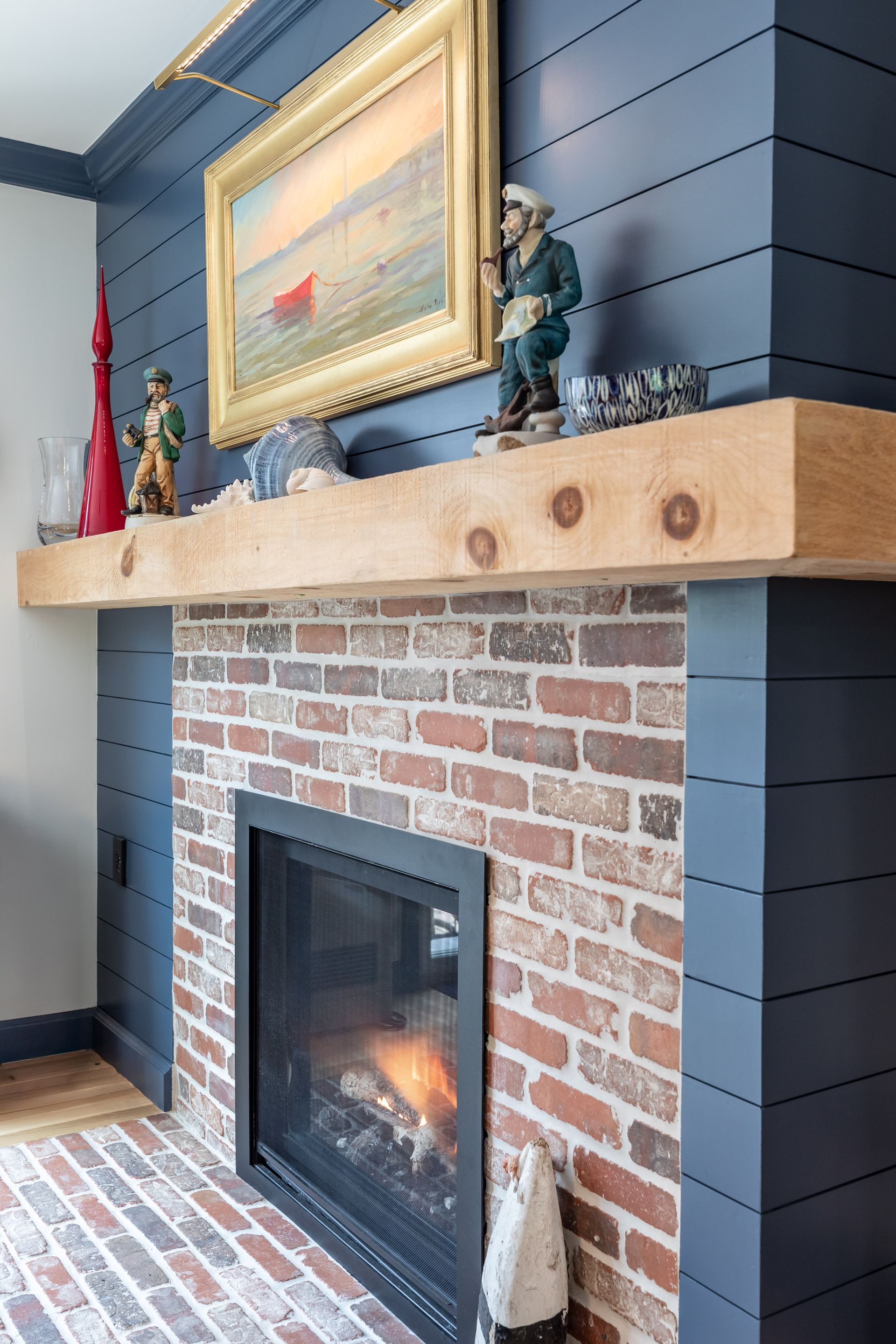 Brick fireplace with black shiplap wall, wood mantel, and a fire burning behind the glass door.
