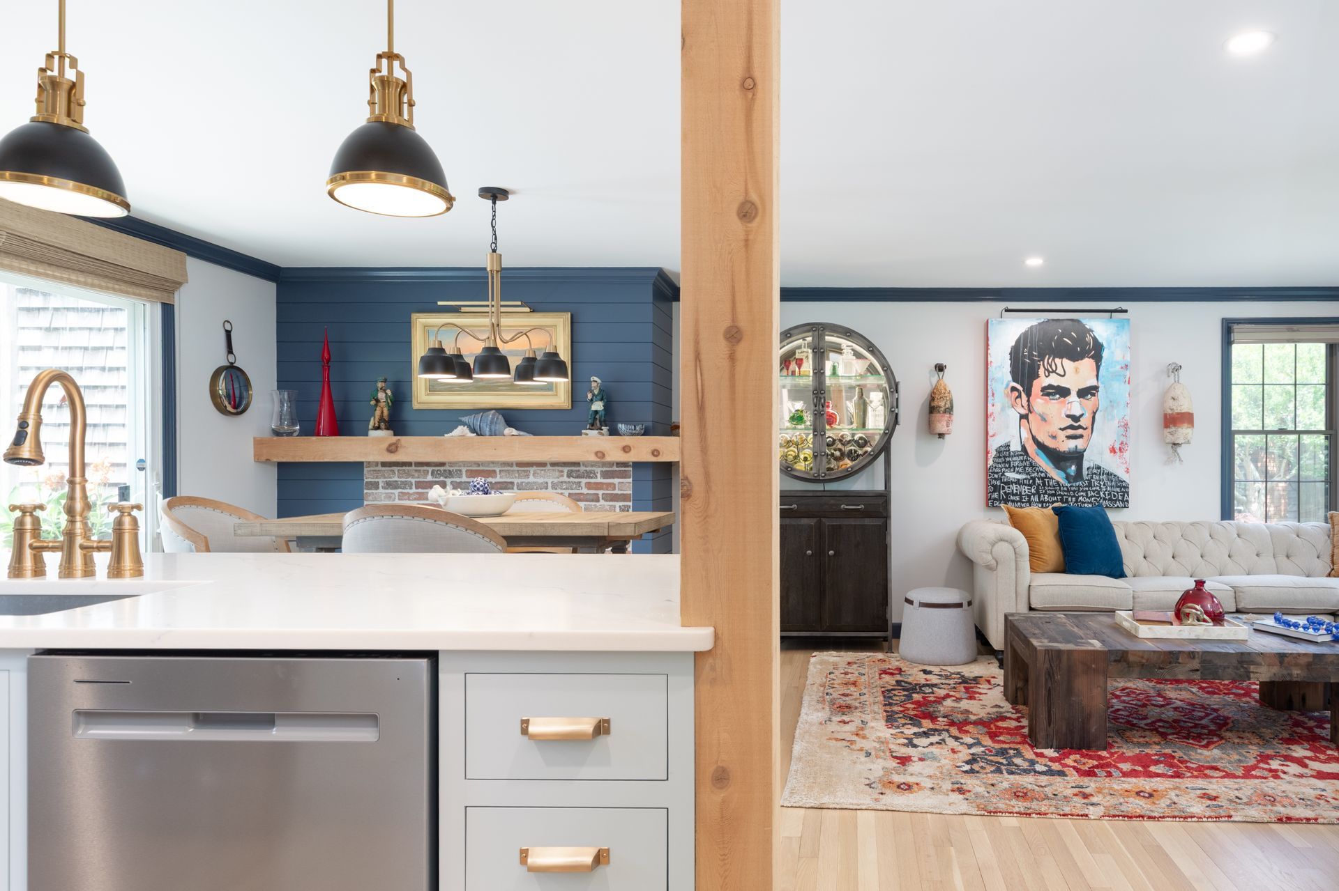 Modern kitchen opening to a cozy living room with blue walls, pendant lights, and a sofa with portrait art.