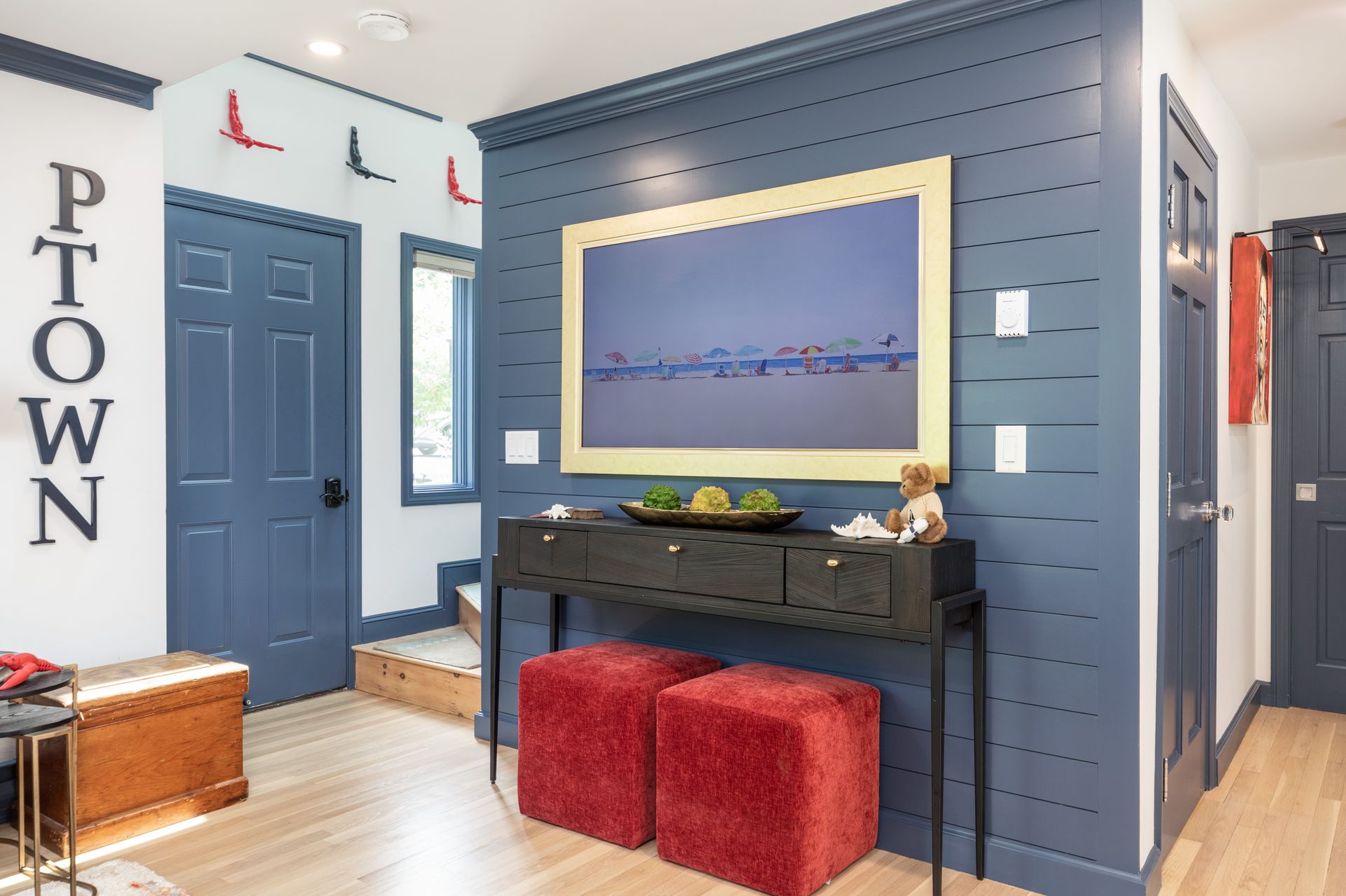 Bright hallway with navy walls, framed art, console table, and red ottomans near the front door