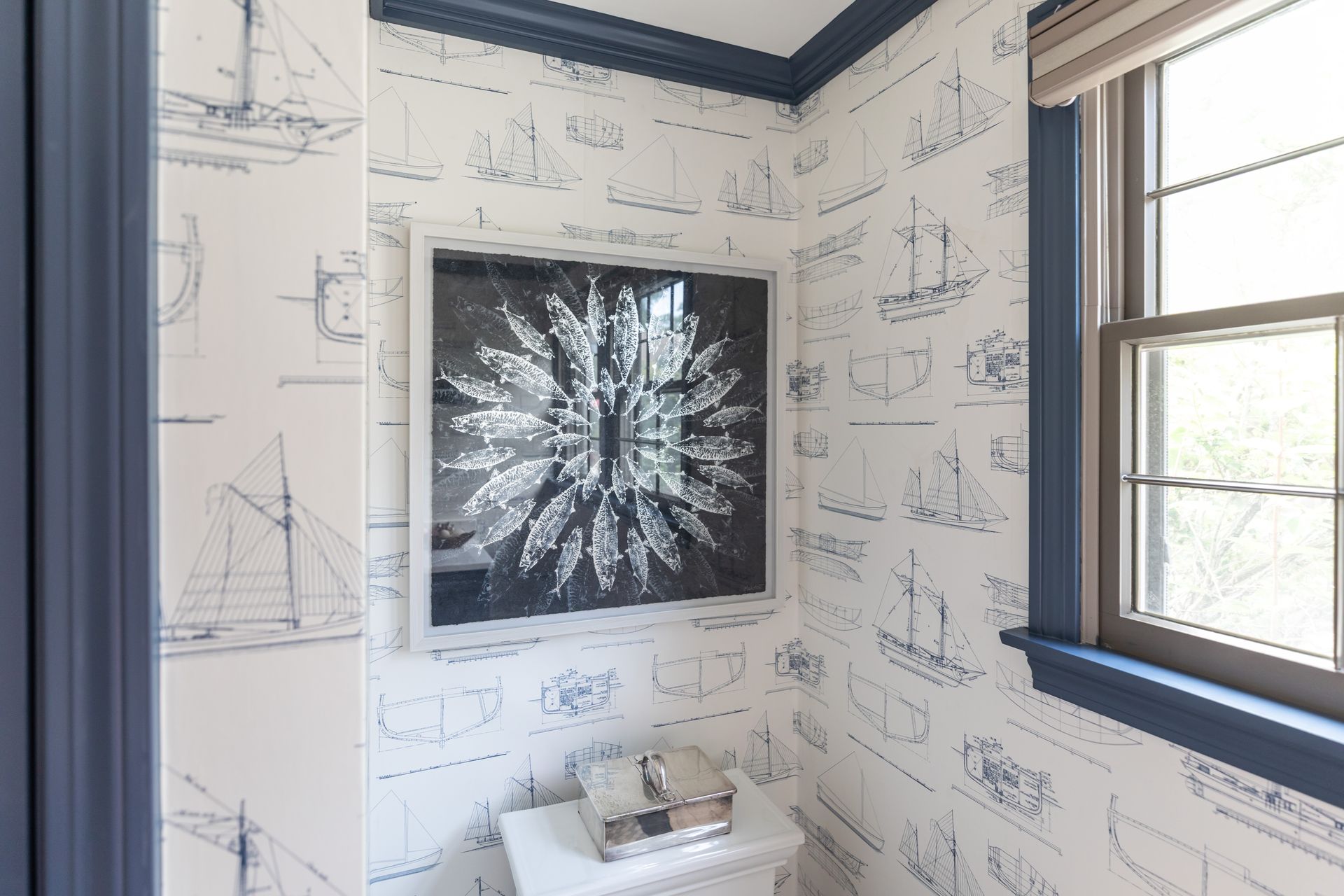 Bathroom with blueprint wallpaper, black-framed abstract wall art, and a window letting in daylight