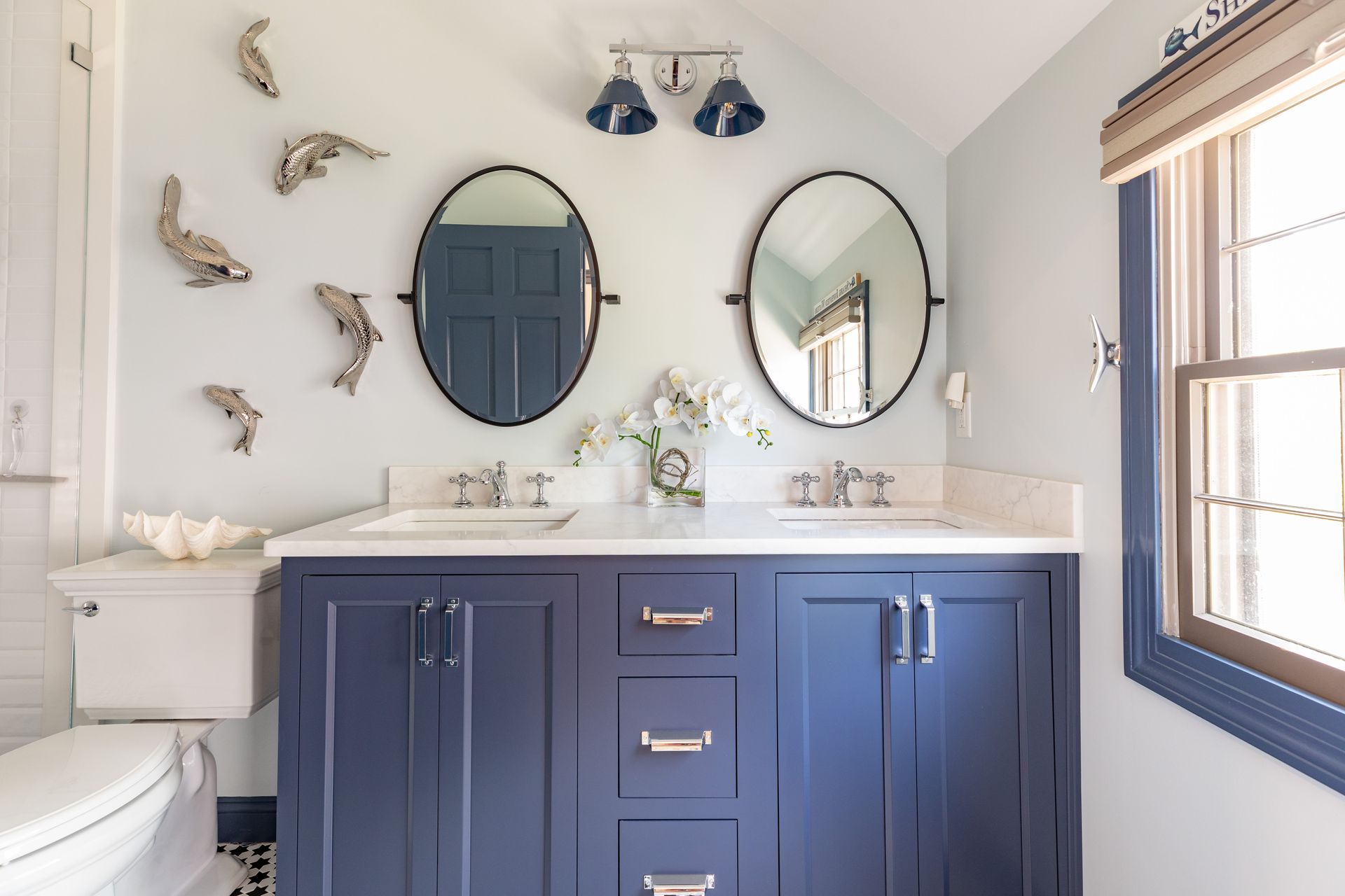 Bright bathroom vanity with navy cabinets, round mirrors, white sink, and blue wall sconces
