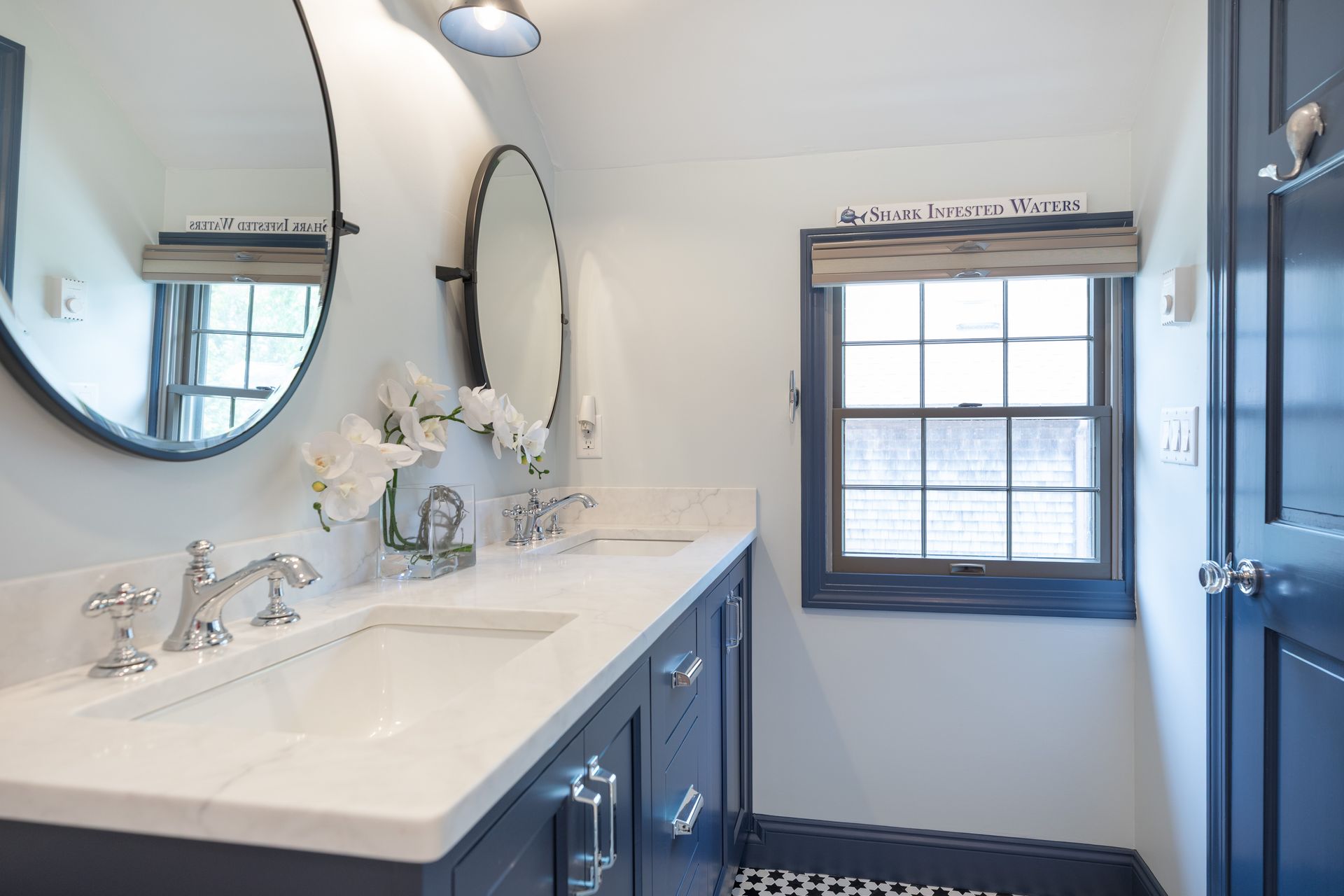 Bright bathroom with double vanity, oval mirror, window, and navy cabinets