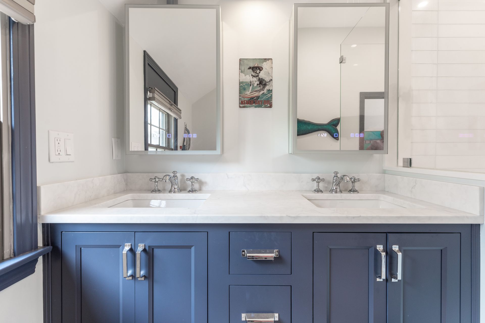 Bathroom vanity with blue cabinets, white countertop, and two mirrors above double sinks