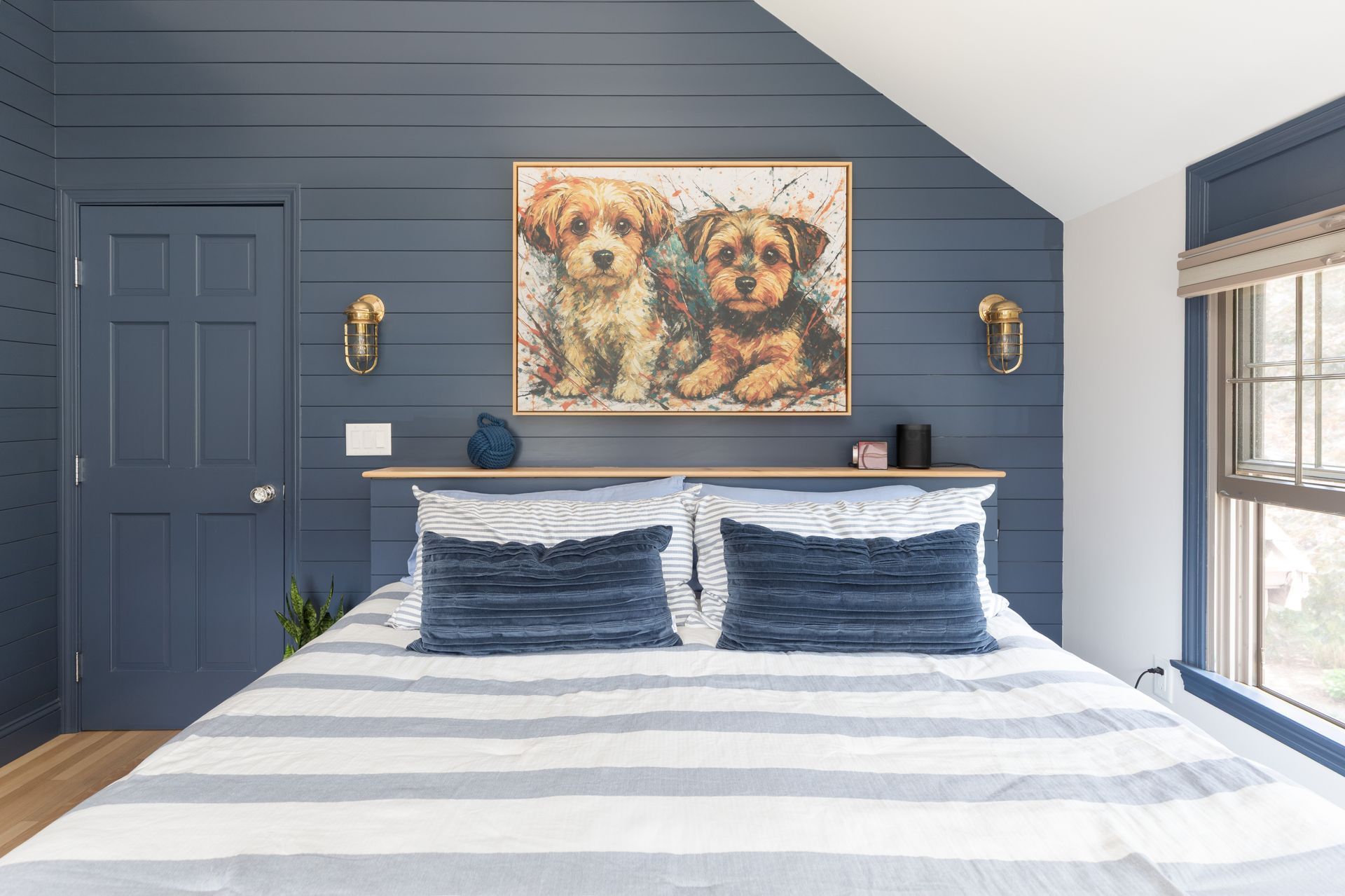Blue bedroom with striped bed, navy walls, window, and dog portrait above the headboard