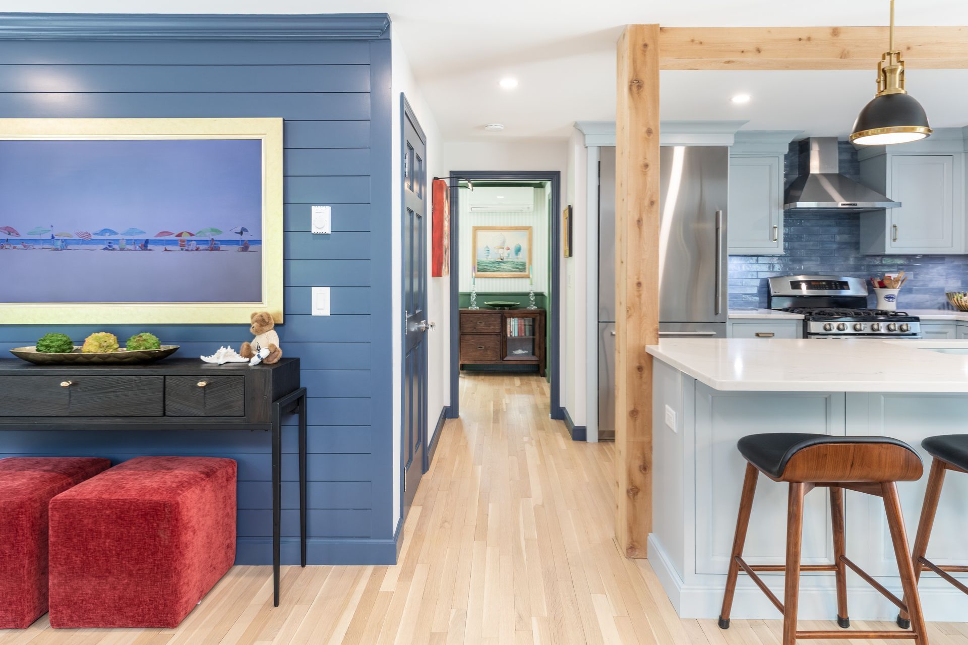 Bright open kitchen and living area with blue accent wall, island stools, and artwork above a console table.