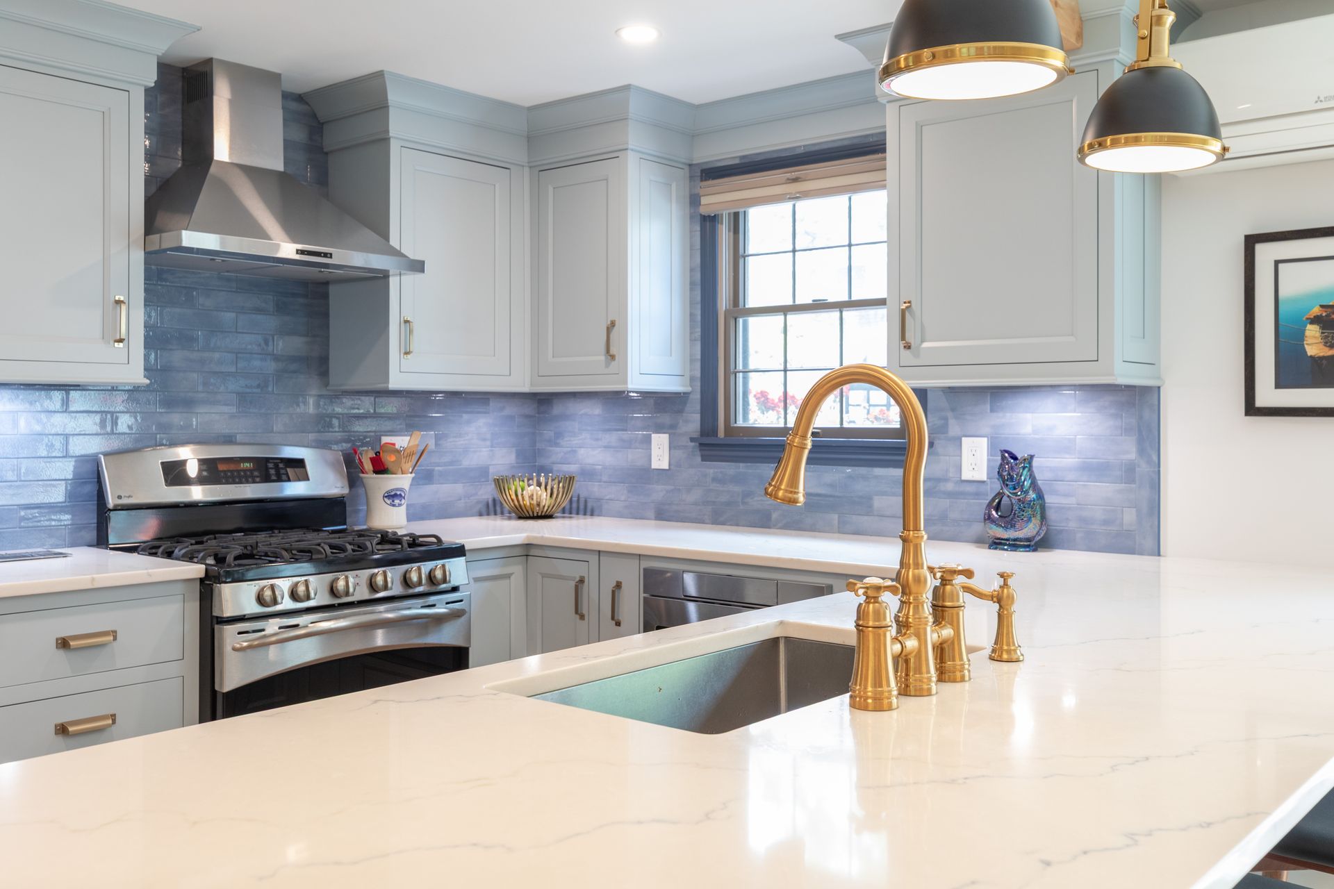 Bright modern kitchen with blue tile backsplash, white cabinets, and a gold faucet over a marble island