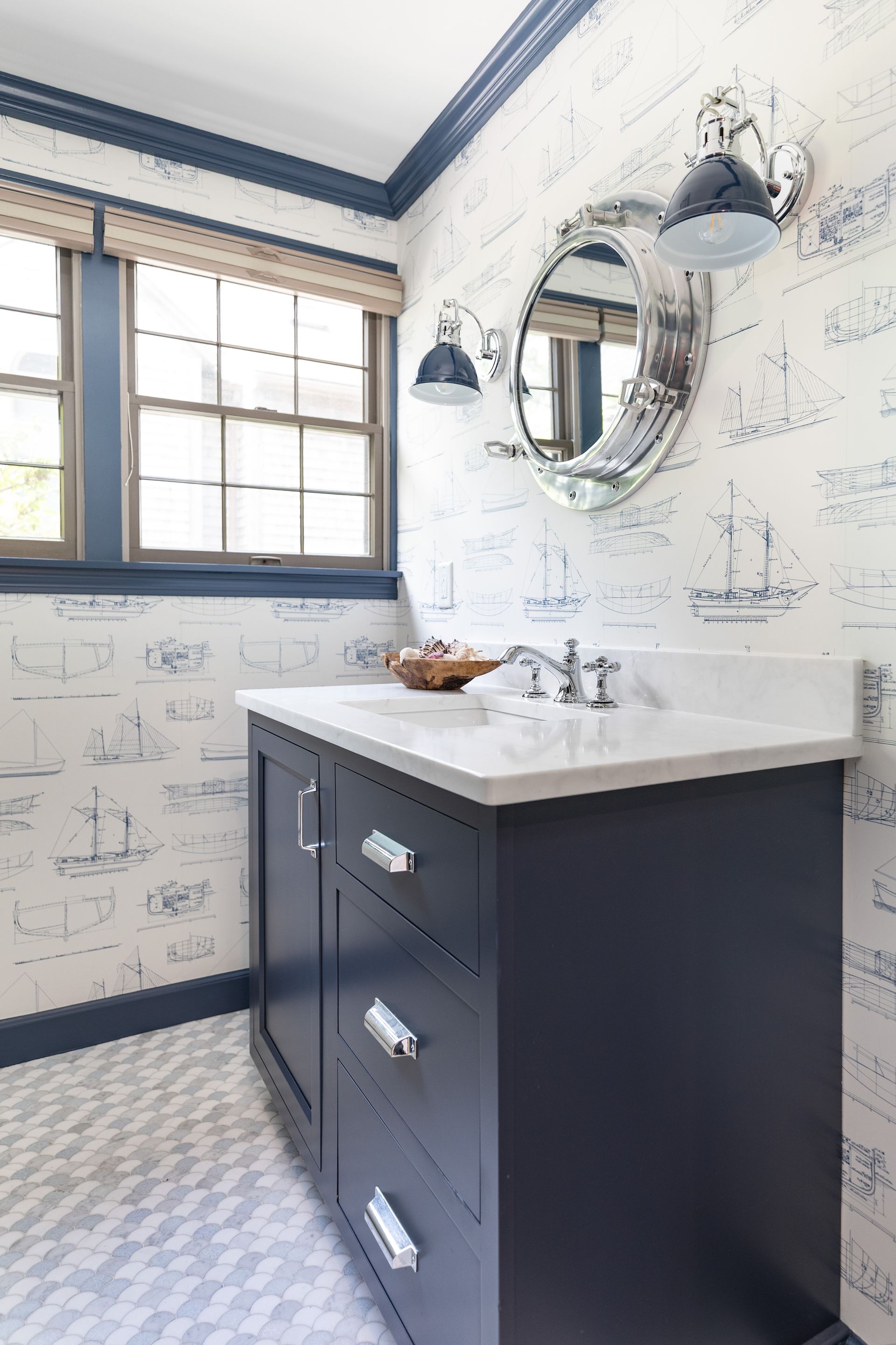 Small bathroom with dark vanity, white countertop, round mirror, and patterned wallpaper and floor tiles.