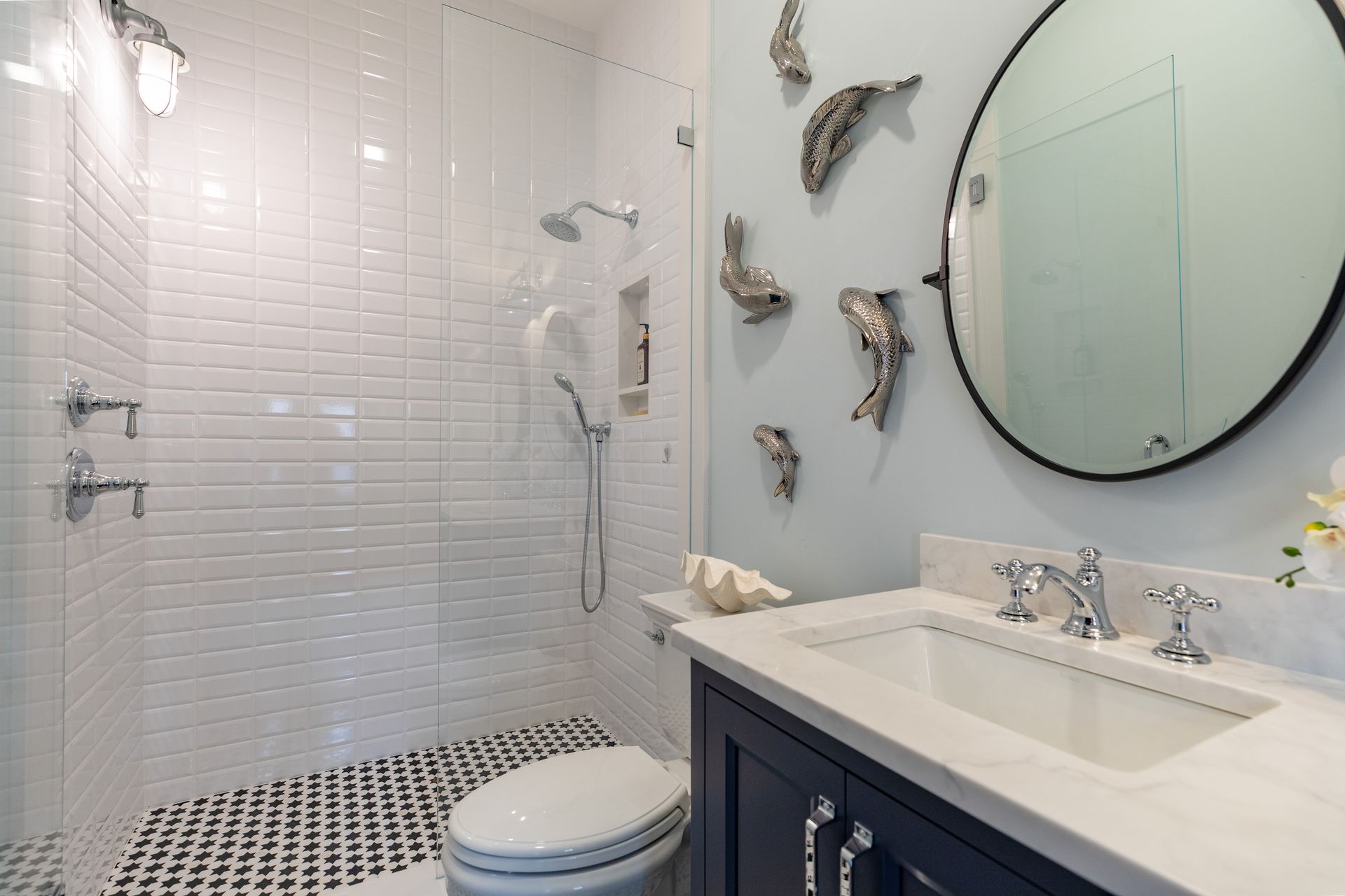 Bright bathroom with white tile shower, black-and-white floor, vanity, and large round mirror