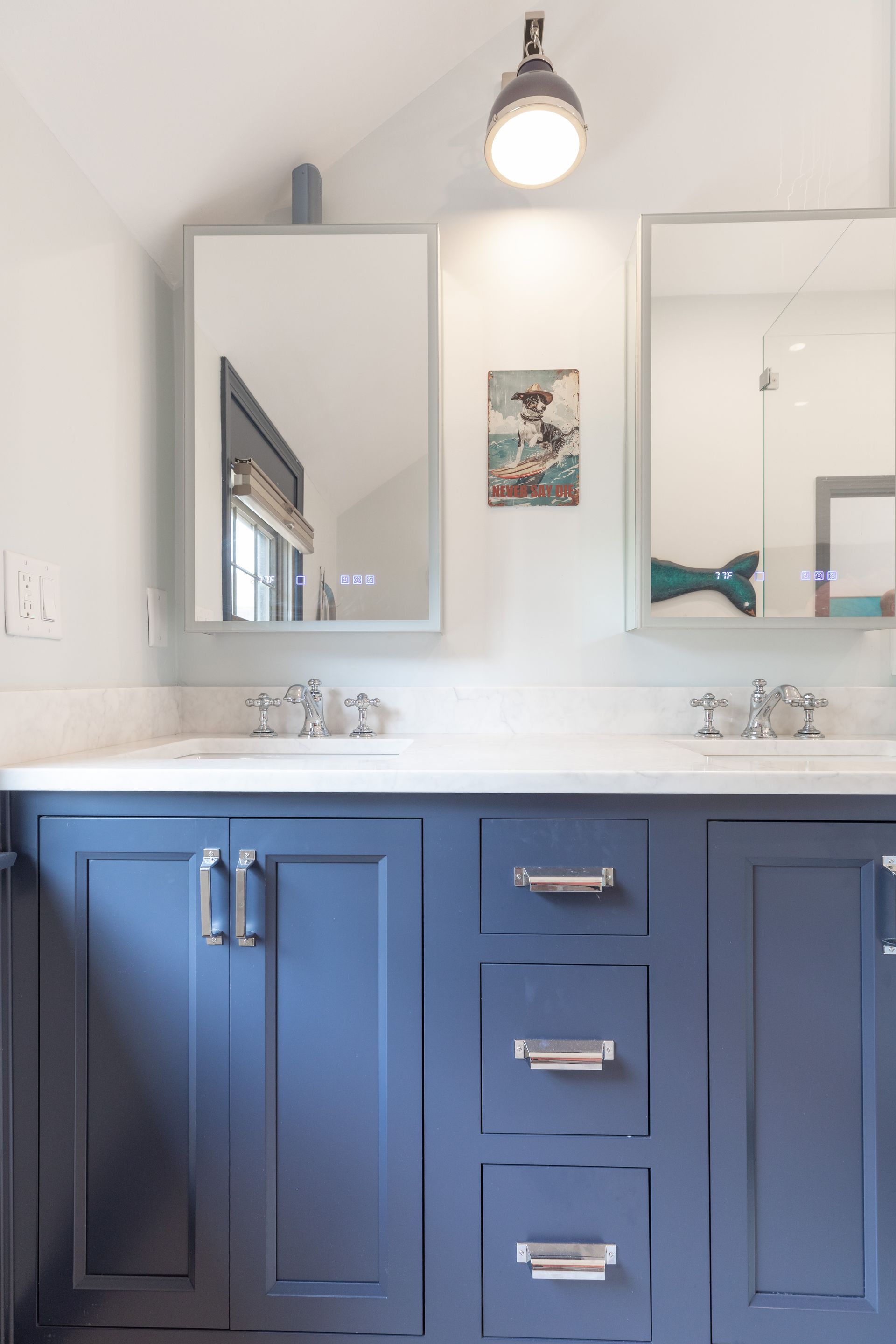 Blue bathroom vanity with white countertop, twin sinks, mirrors, and a single pendant light