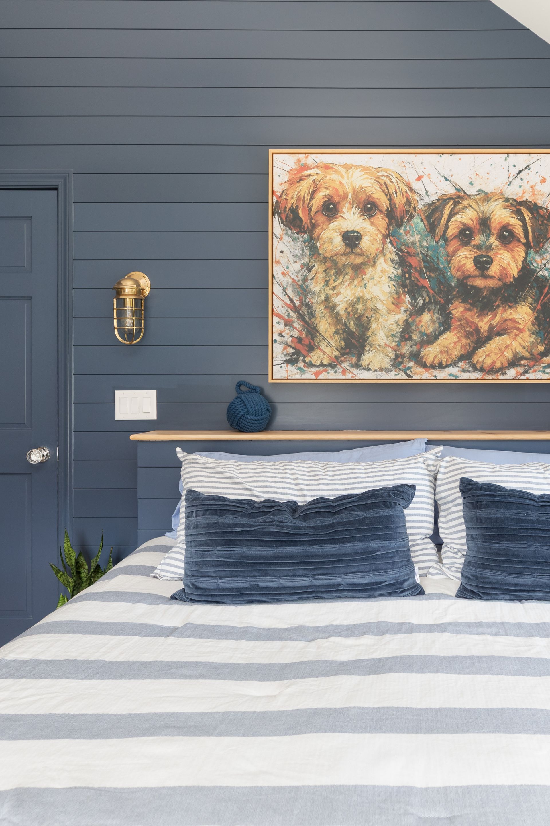 Bedroom with navy paneled wall, striped bed, and framed dog portrait above the headboard