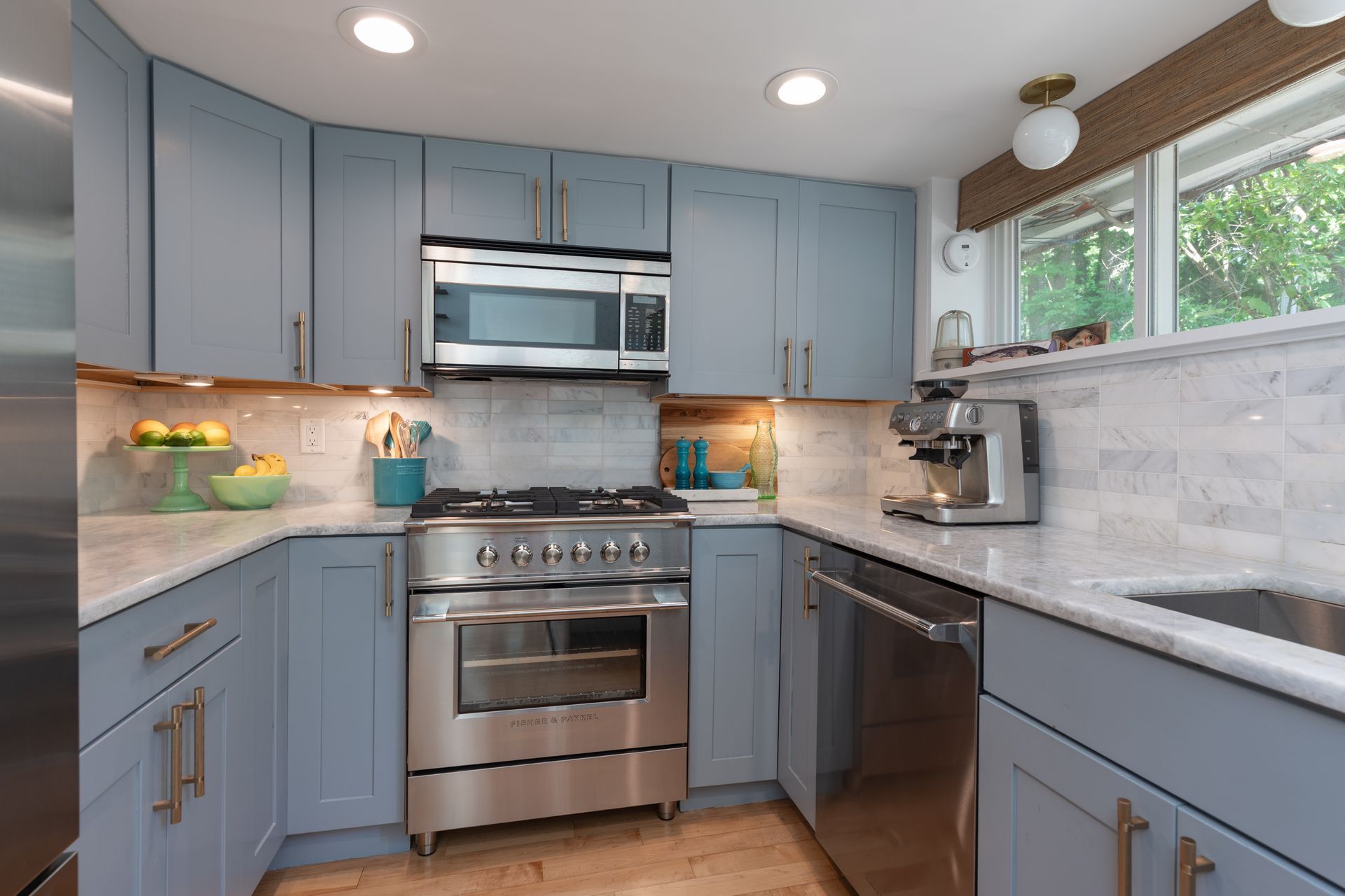 Bright modern kitchen with blue cabinets, stainless steel appliances, white countertops, and a window above the sink