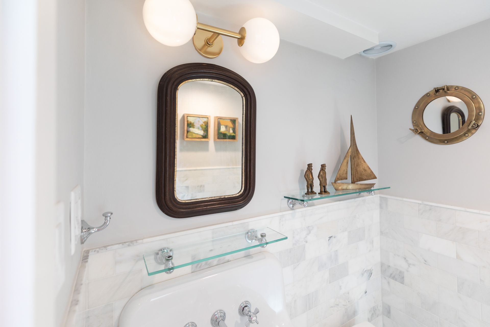 Bright bathroom with oval mirror, glass shelf, wall sconces, and white tiled walls