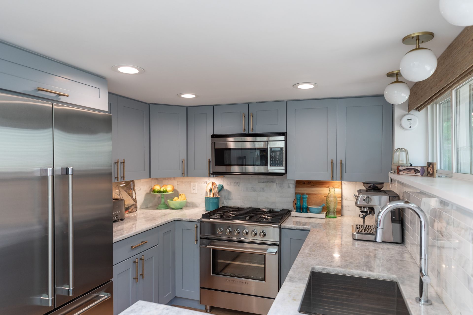 Bright modern kitchen with stainless steel appliances, gray cabinets, marble counters, and a window over the sink