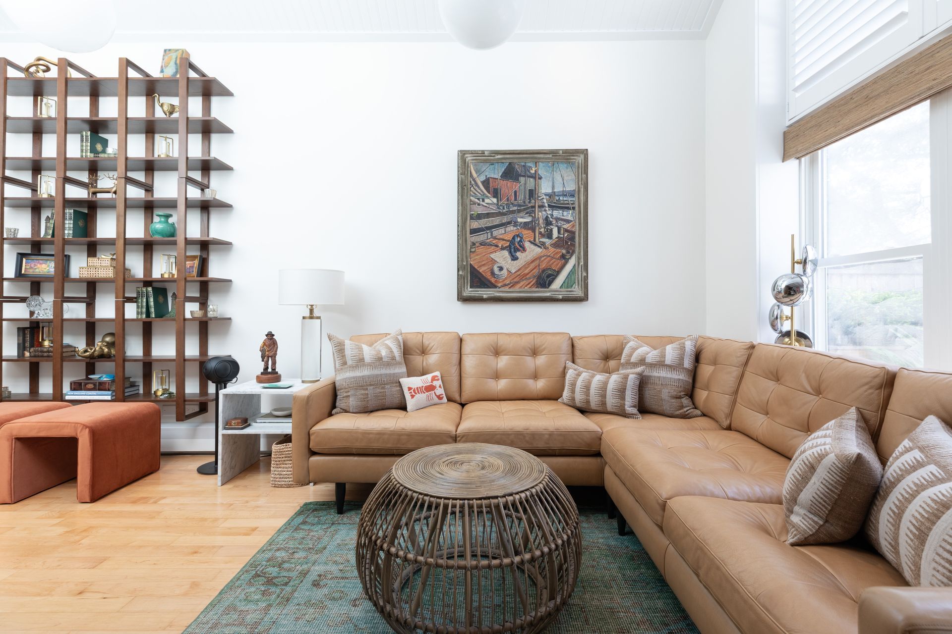 Bright living room with tan sectional sofa, woven coffee table, bookshelf divider, and large windows