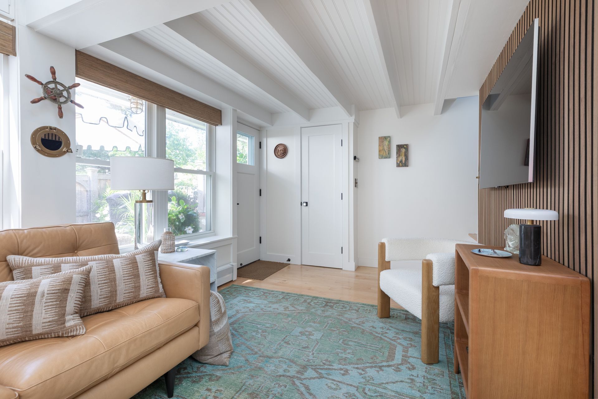 Bright living room with tan sofa, blue rug, white walls, and TV on a wooden console.